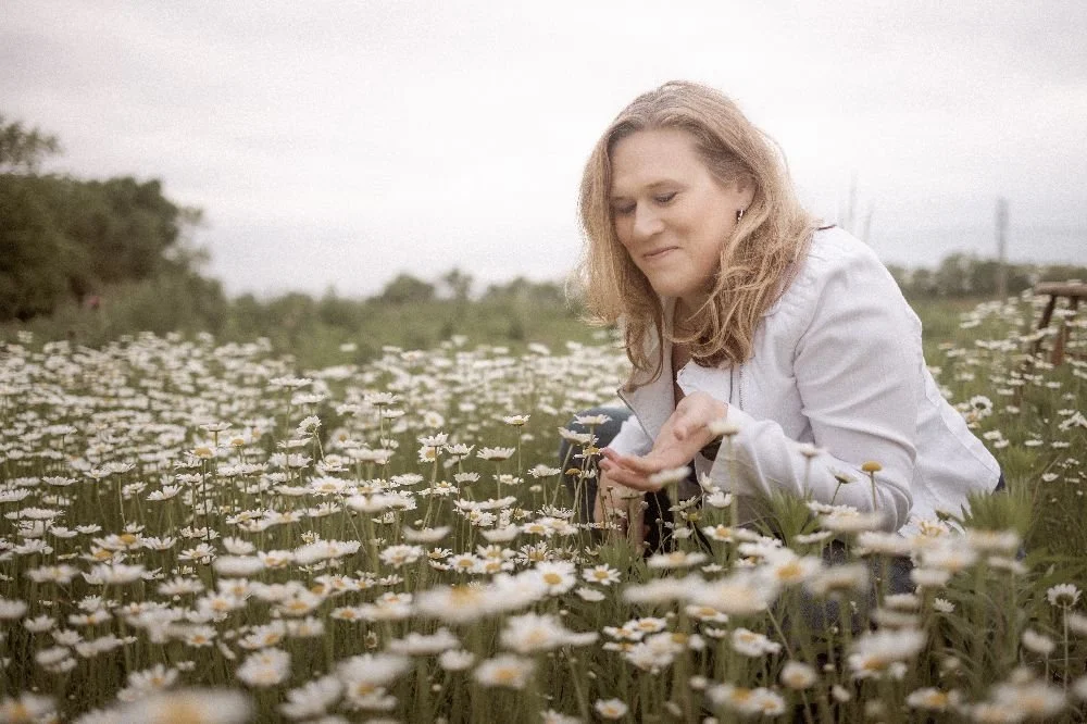 Picture of a woman squatting in a field of white and yellow flowers in Kansas