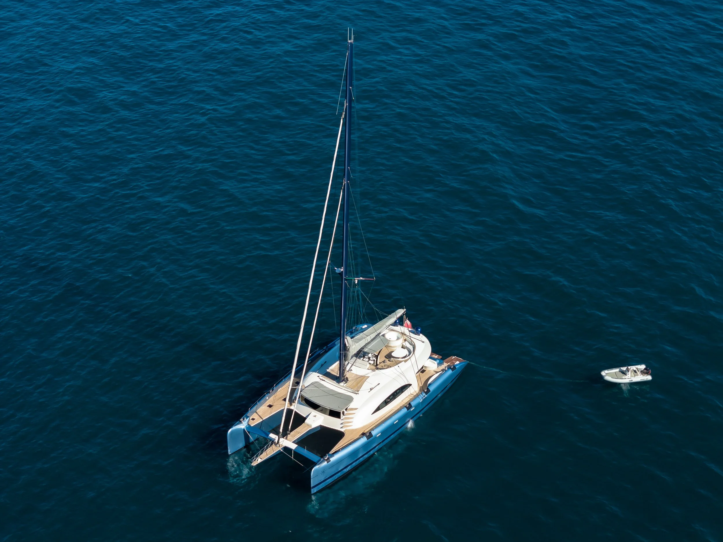 Aerial view of a large white yacht with a smaller boat nearby, floating on blue ocean water. LYFE AT SEA