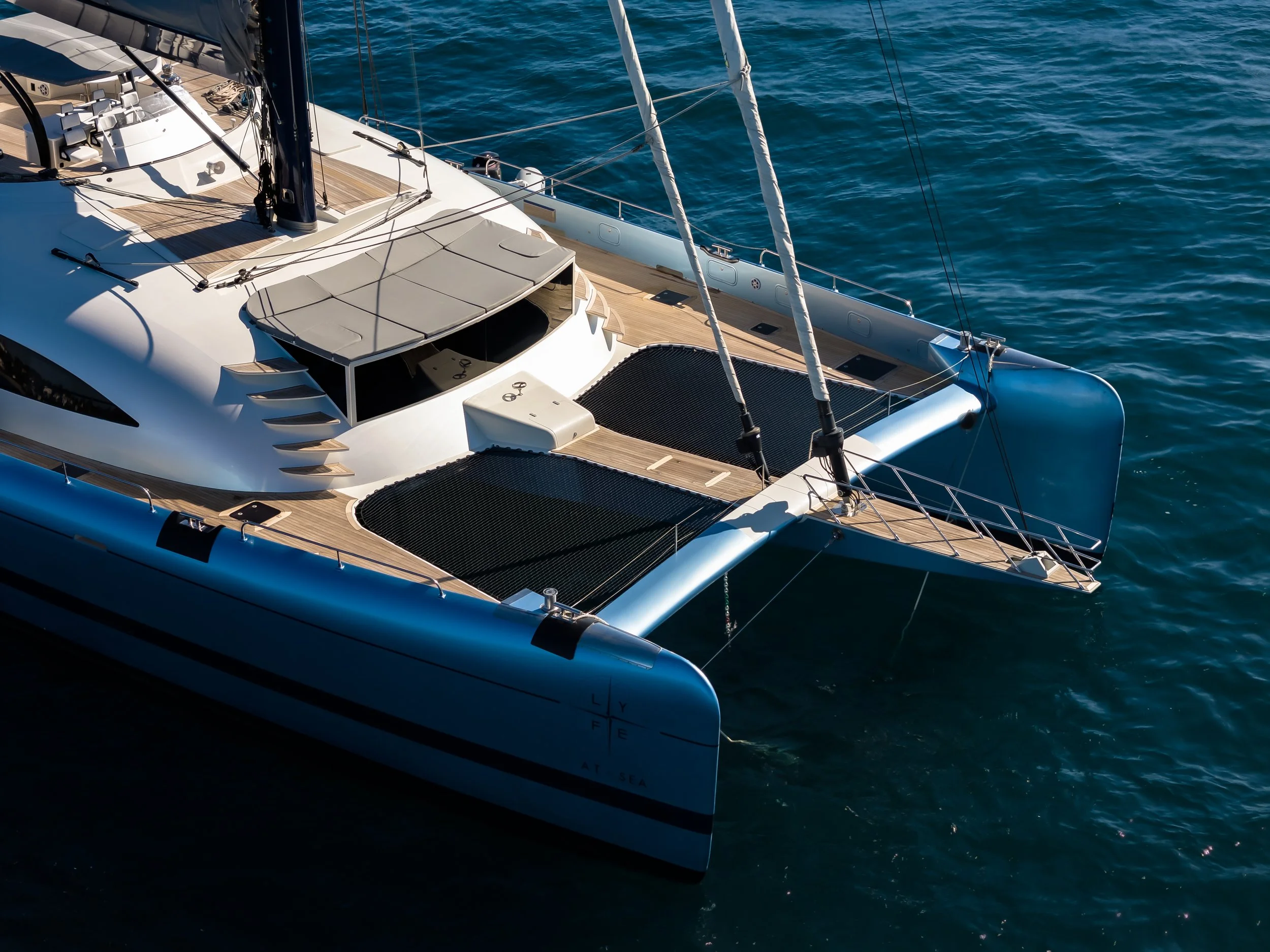 A luxury sailing yacht floating on calm blue water, showing the deck, rigging, and part of the hull. LYFE AT SEA