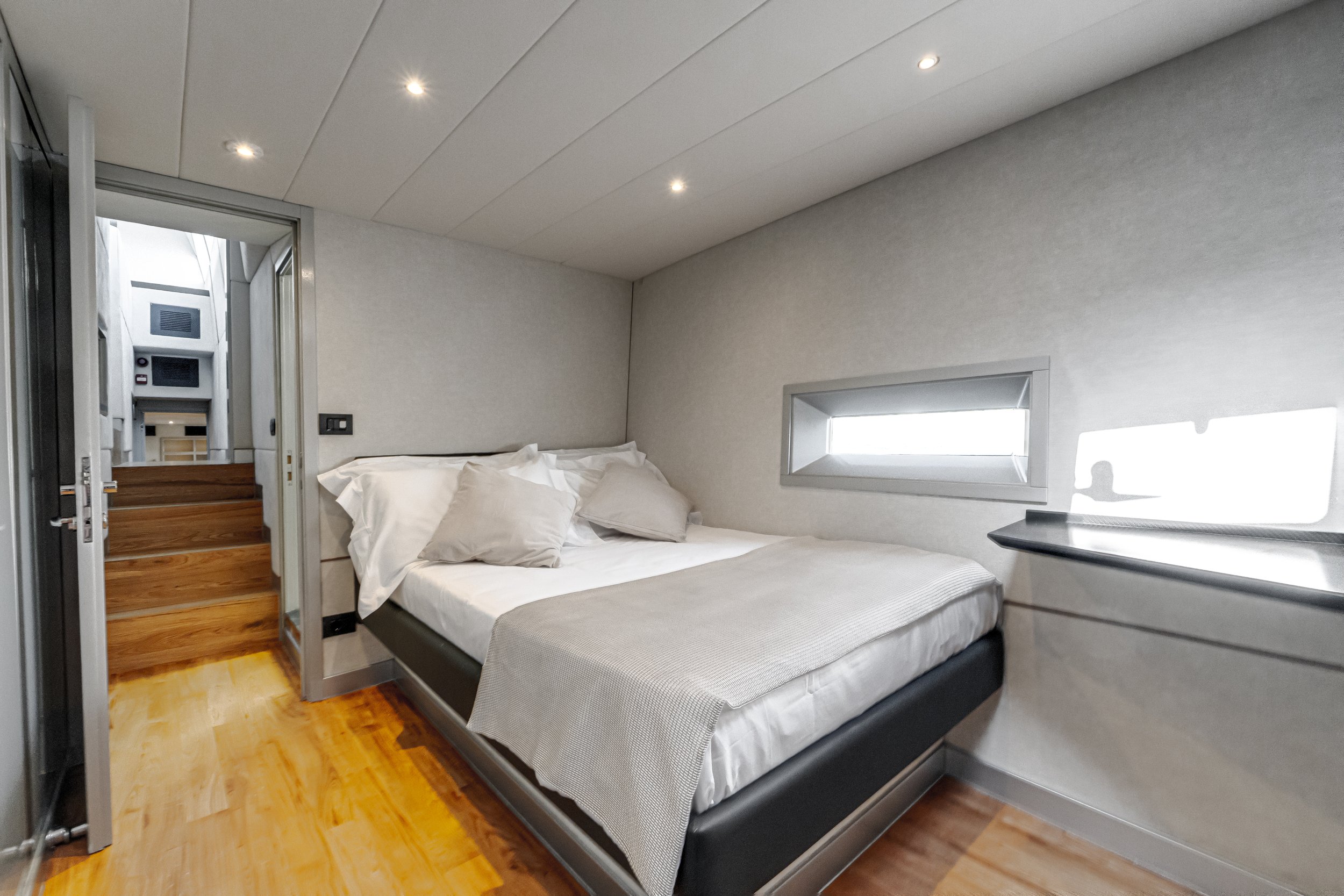 Interior of a modern bedroom with a bed, pillows, a small window, and ceiling lights.