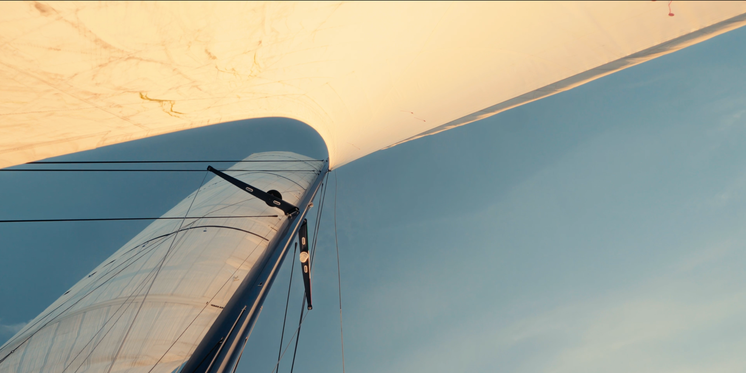 Close-up view of a sailboat's mast and sail against a blue sky. LYFE AT SEA
