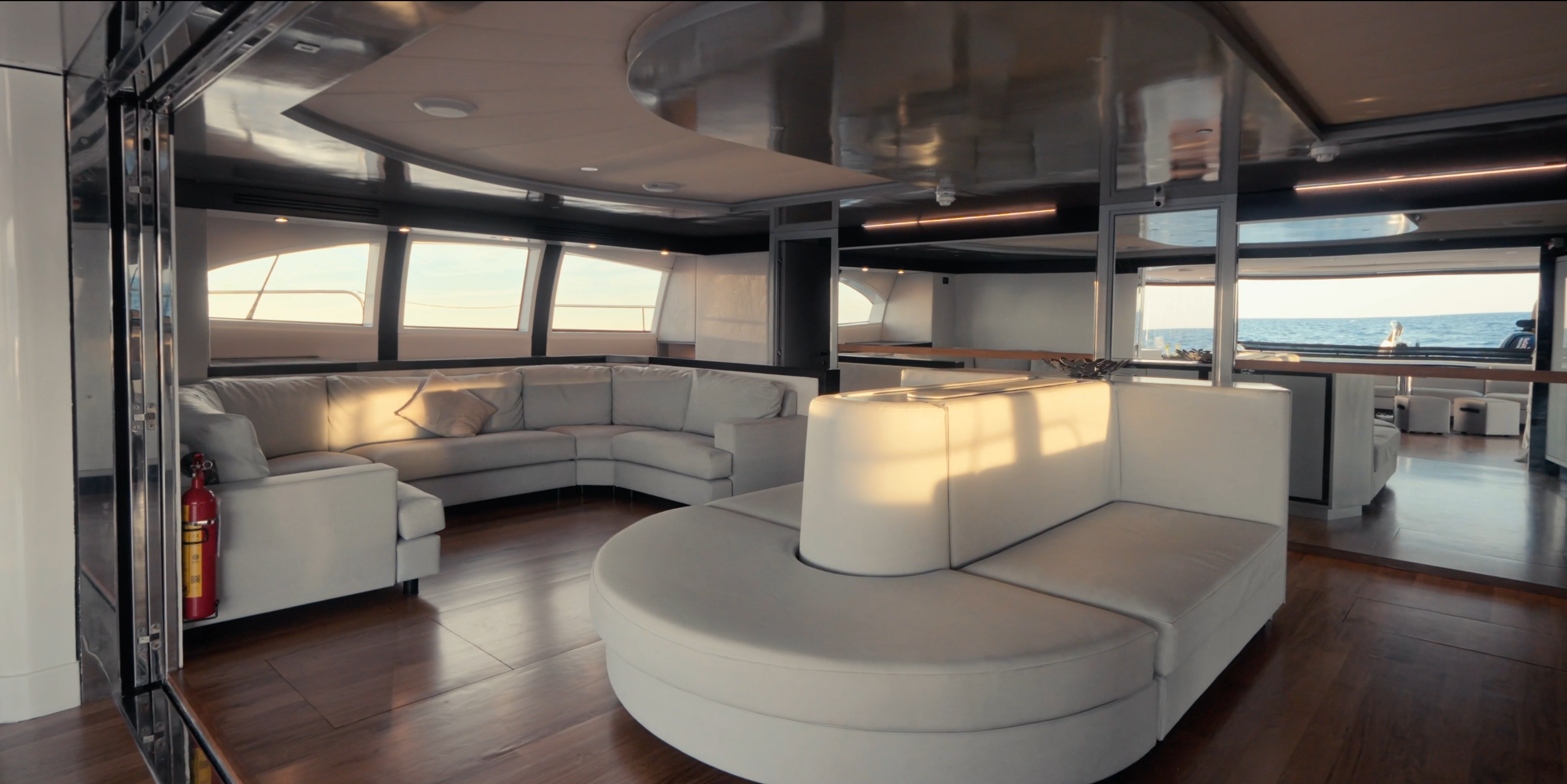 Interior of a yacht with white leather couches and large windows showing the ocean outside. LYFE AT SEA