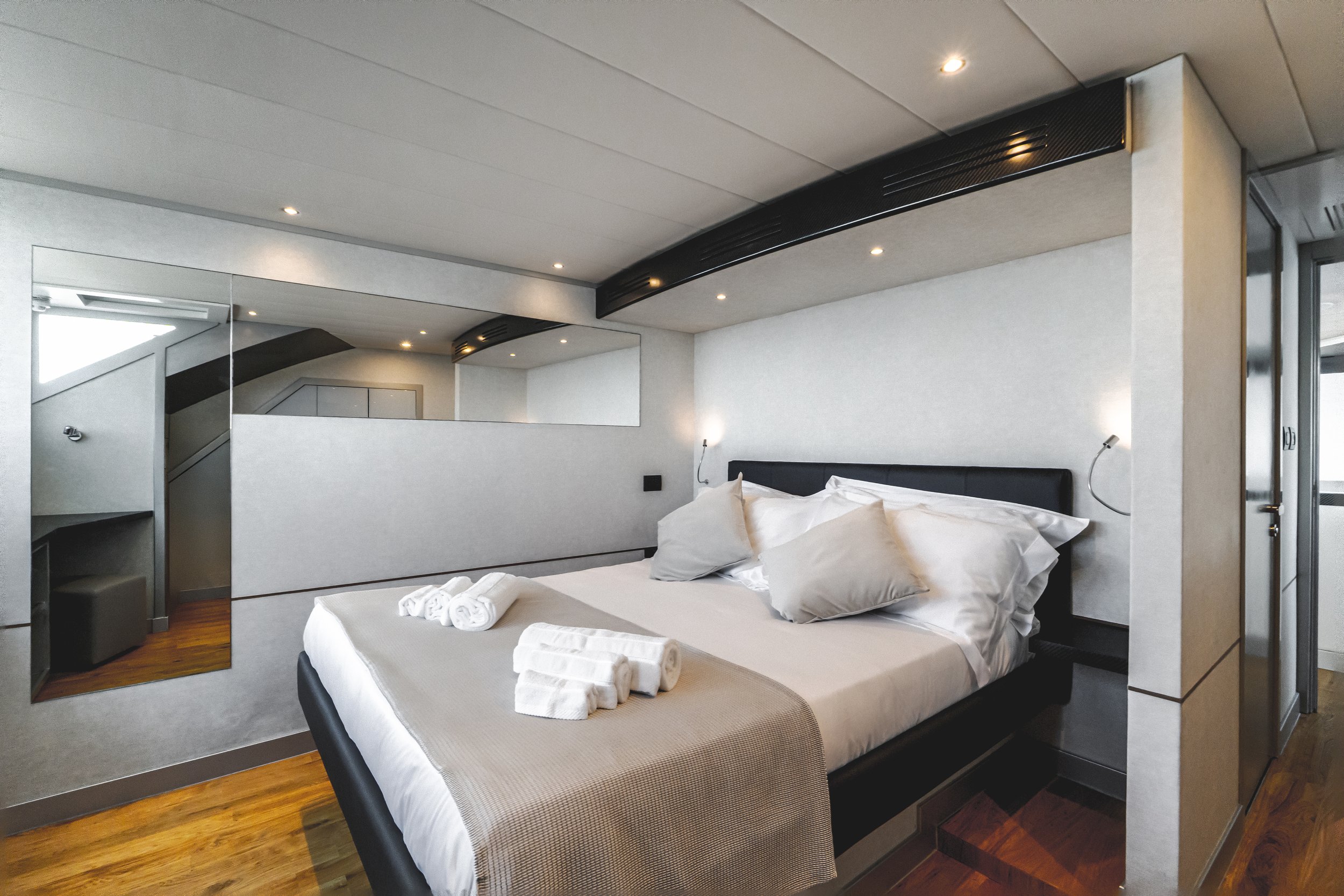 Modern hotel room with a large bed, white bedding, rolled towels, a bedside lamp, a mirror, and a balcony door- LYFE AT SEA