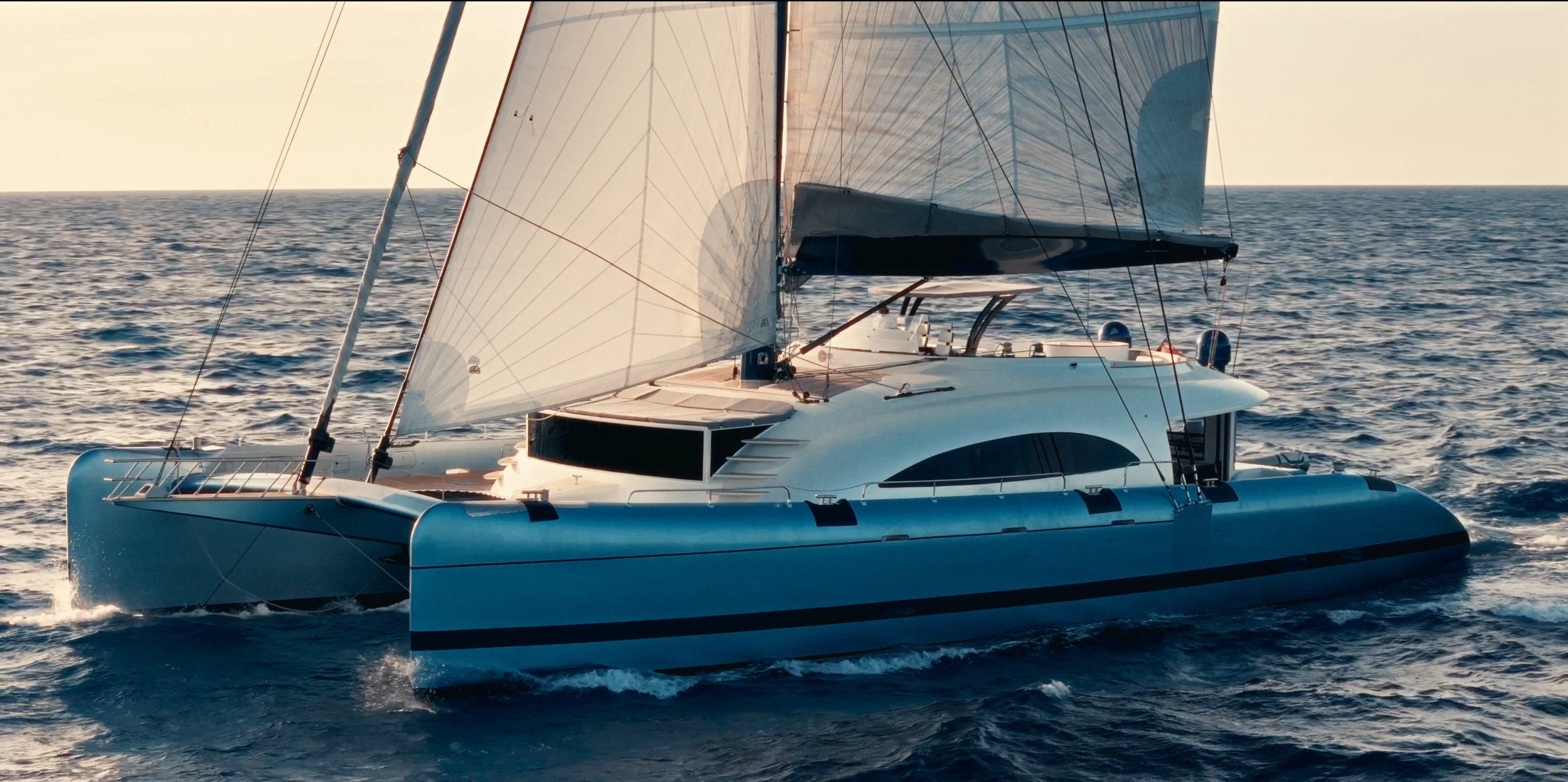 A modern sailboat with white sails sailing on the open ocean during sunset. LYFE AT SEA