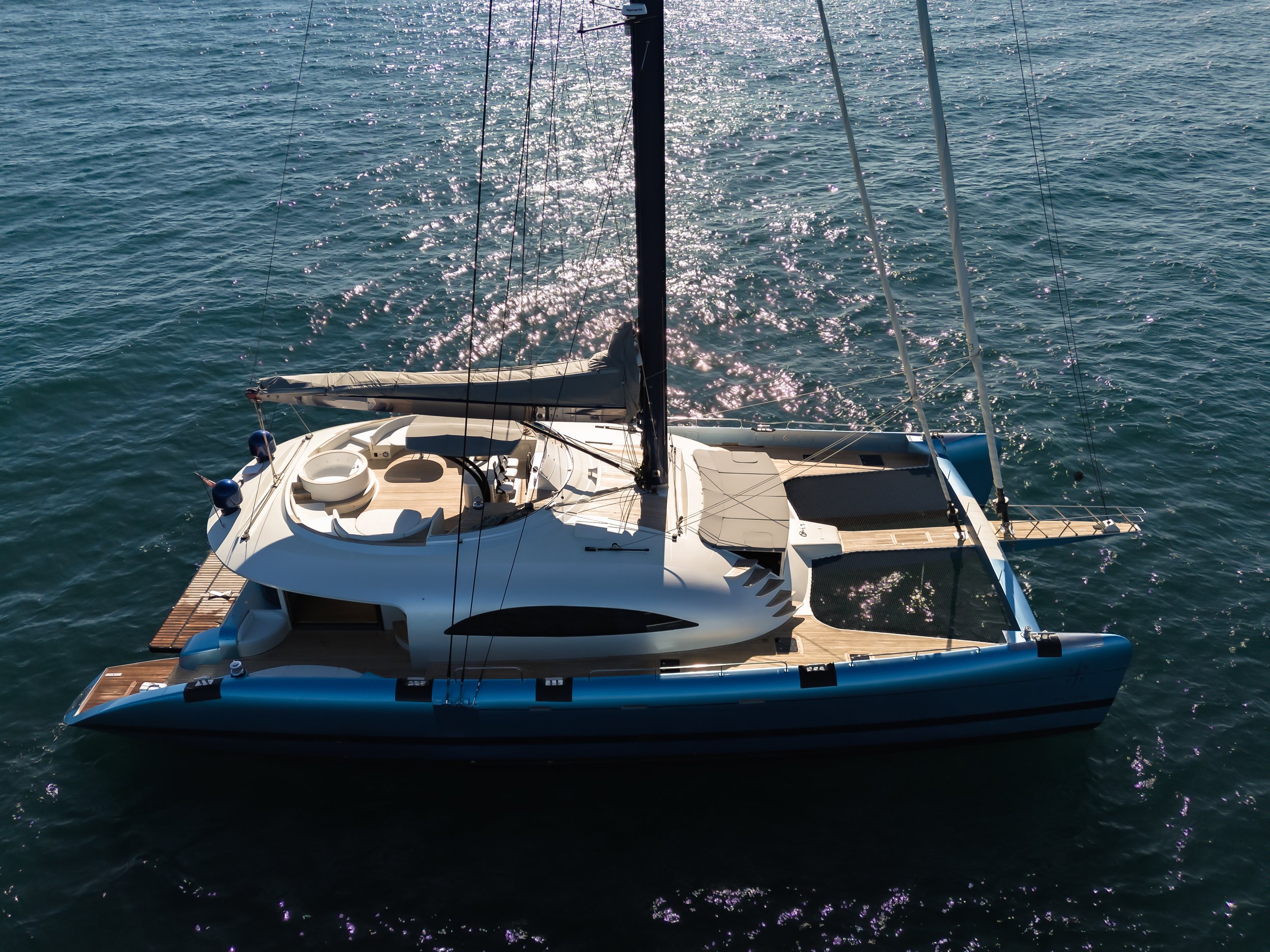 A white yacht sailboat on the water with the sun reflecting off the surface, showing the deck, sail, and rigging. LYFE AT SEA