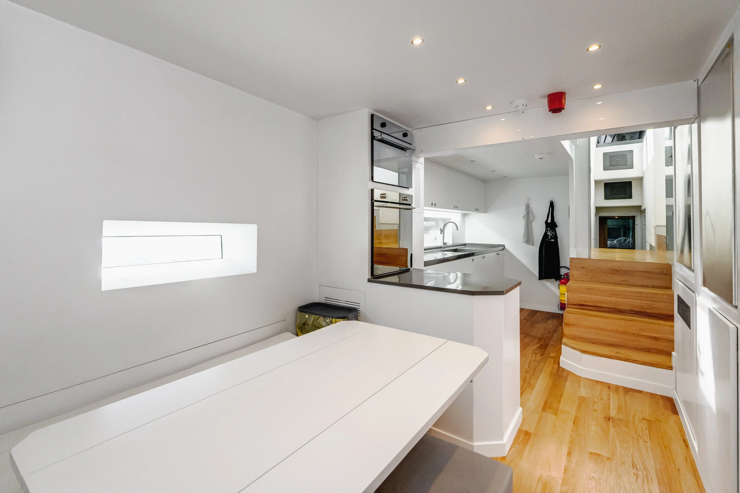 Modern kitchen with white countertops, cabinets, and a wooden floor, with a staircase leading upstairs. LYFE AT SEA