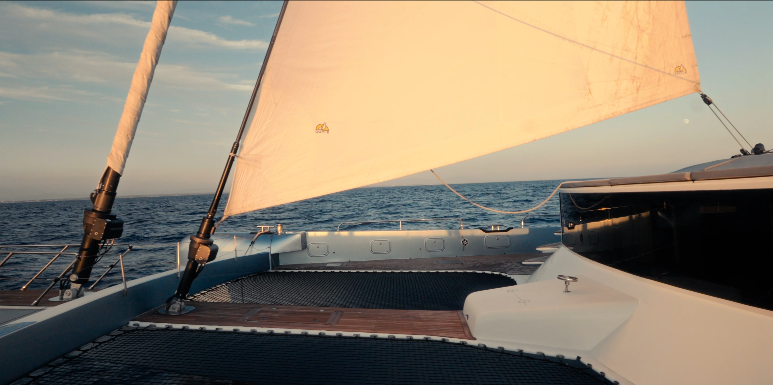 View from a sailboat during sunset, showing sails, ocean, and clear sky. LYFE AT SEA