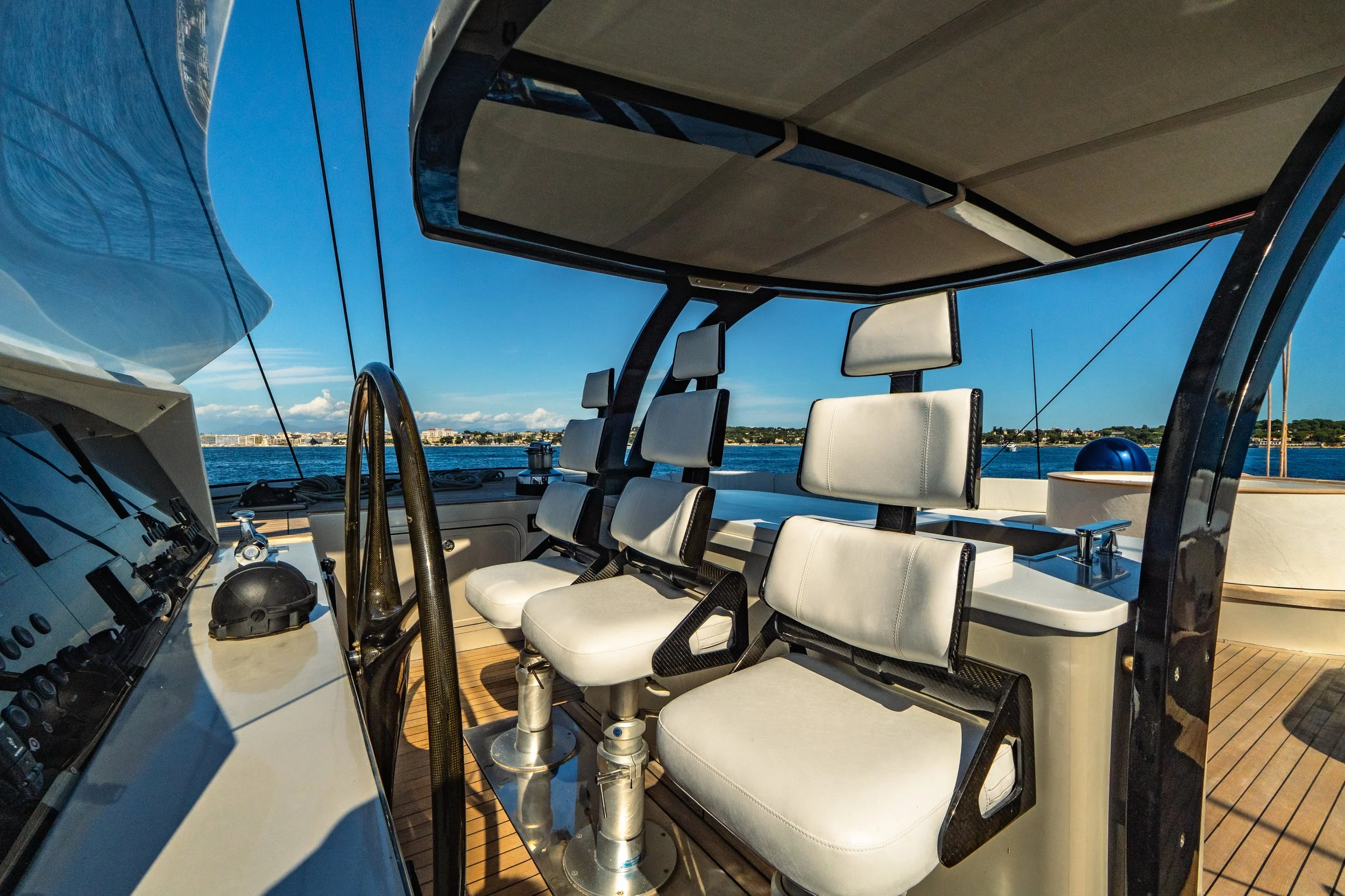 View of the cockpit on a yacht overlooking the water and a distant shoreline with buildings.