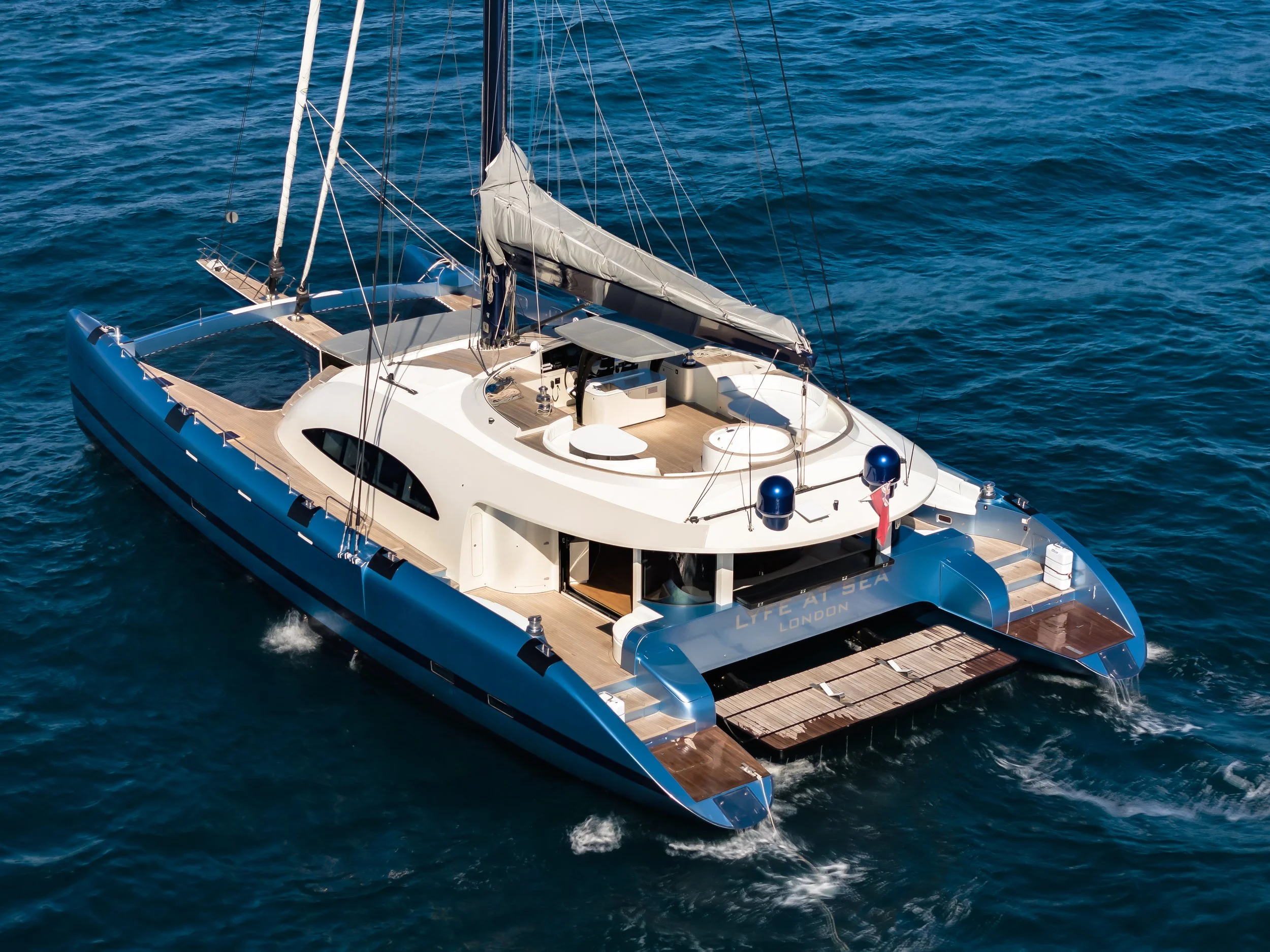 A luxury white sailing yacht with multiple decks and masts sailing in open blue water.