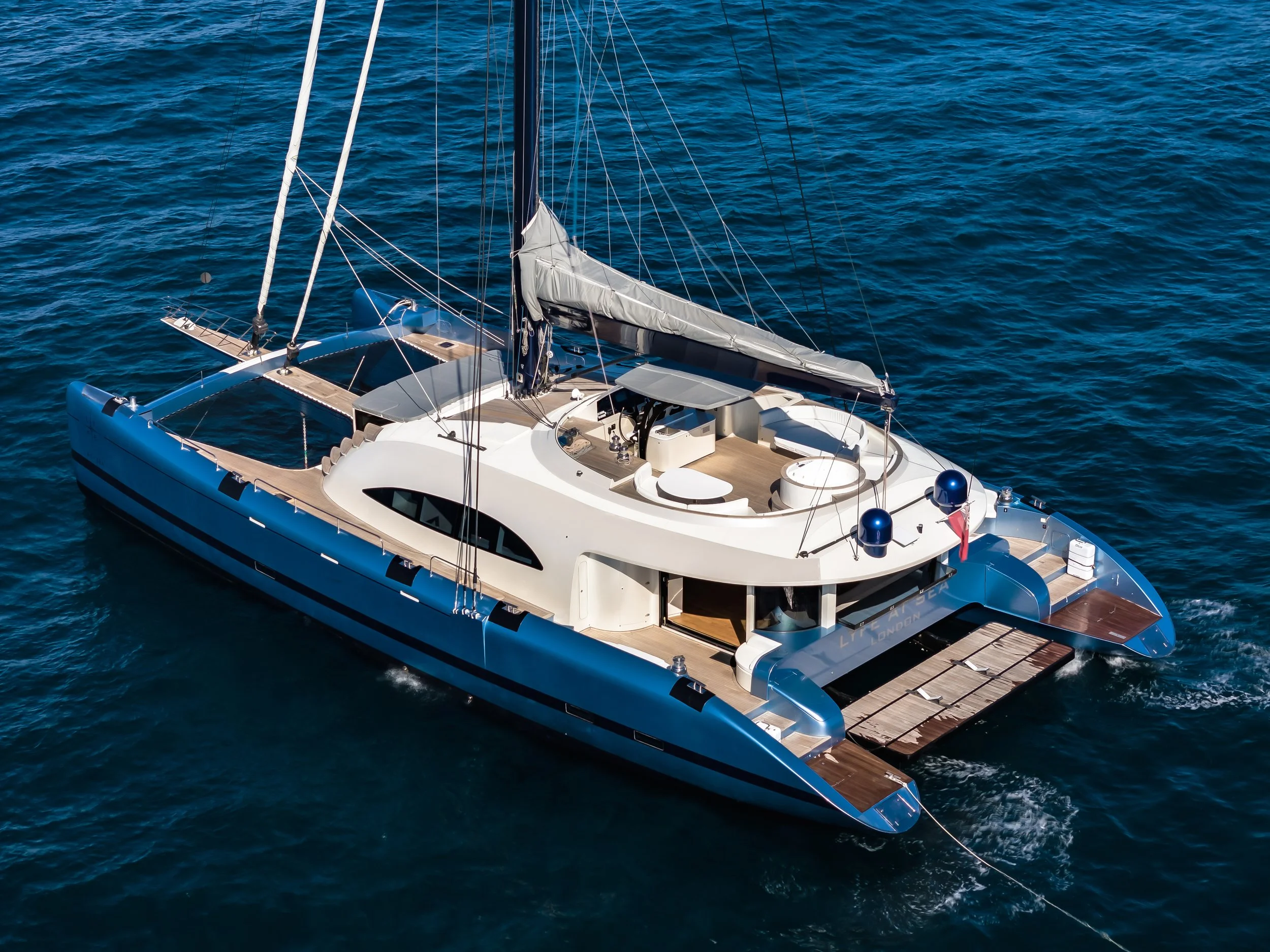 An aerial view of a modern yacht with white and blue colors floating on the deep blue ocean water.