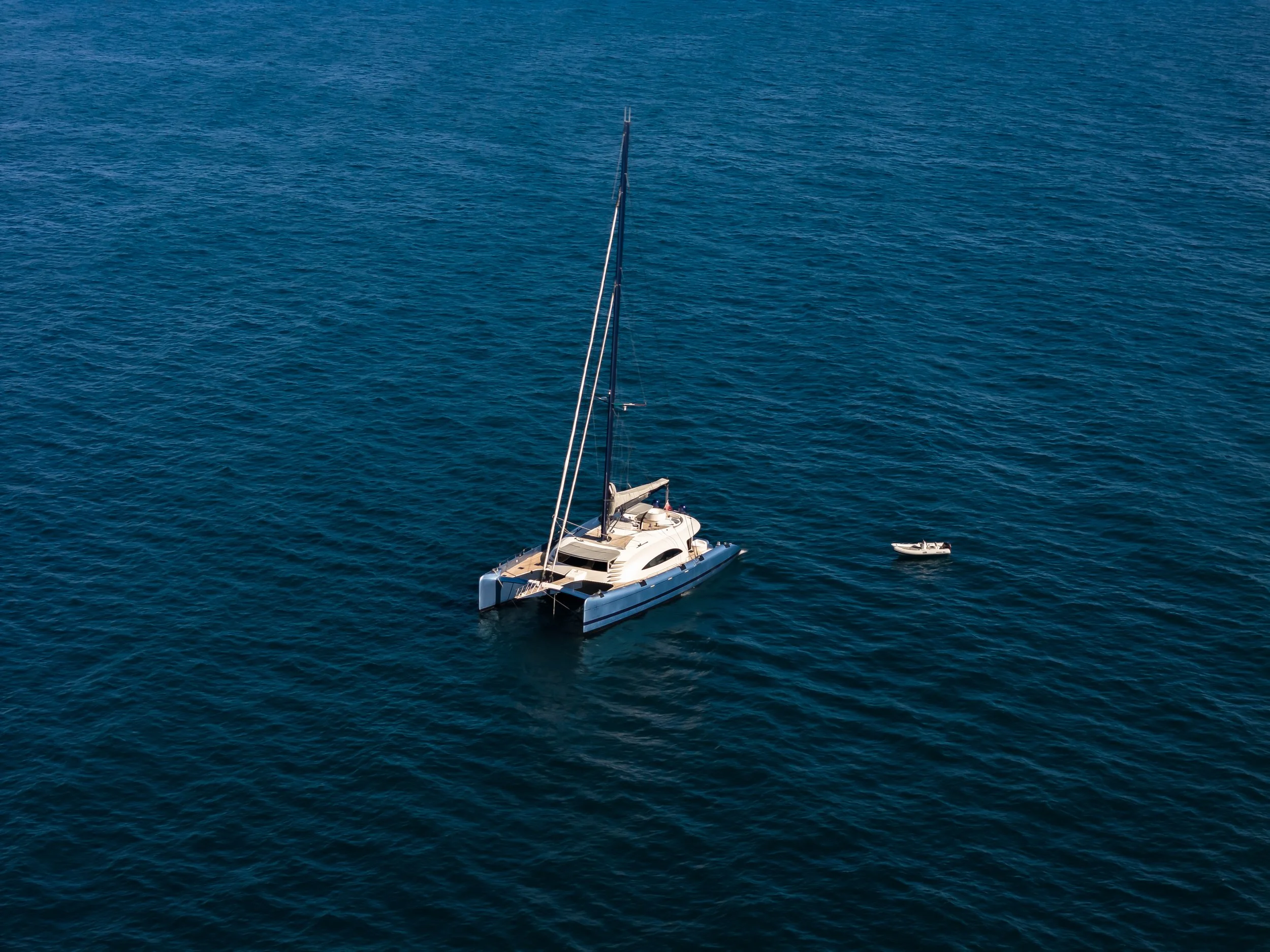 A sailboat floating on calm blue water with a small motorboat nearby. LYFE AT SEA