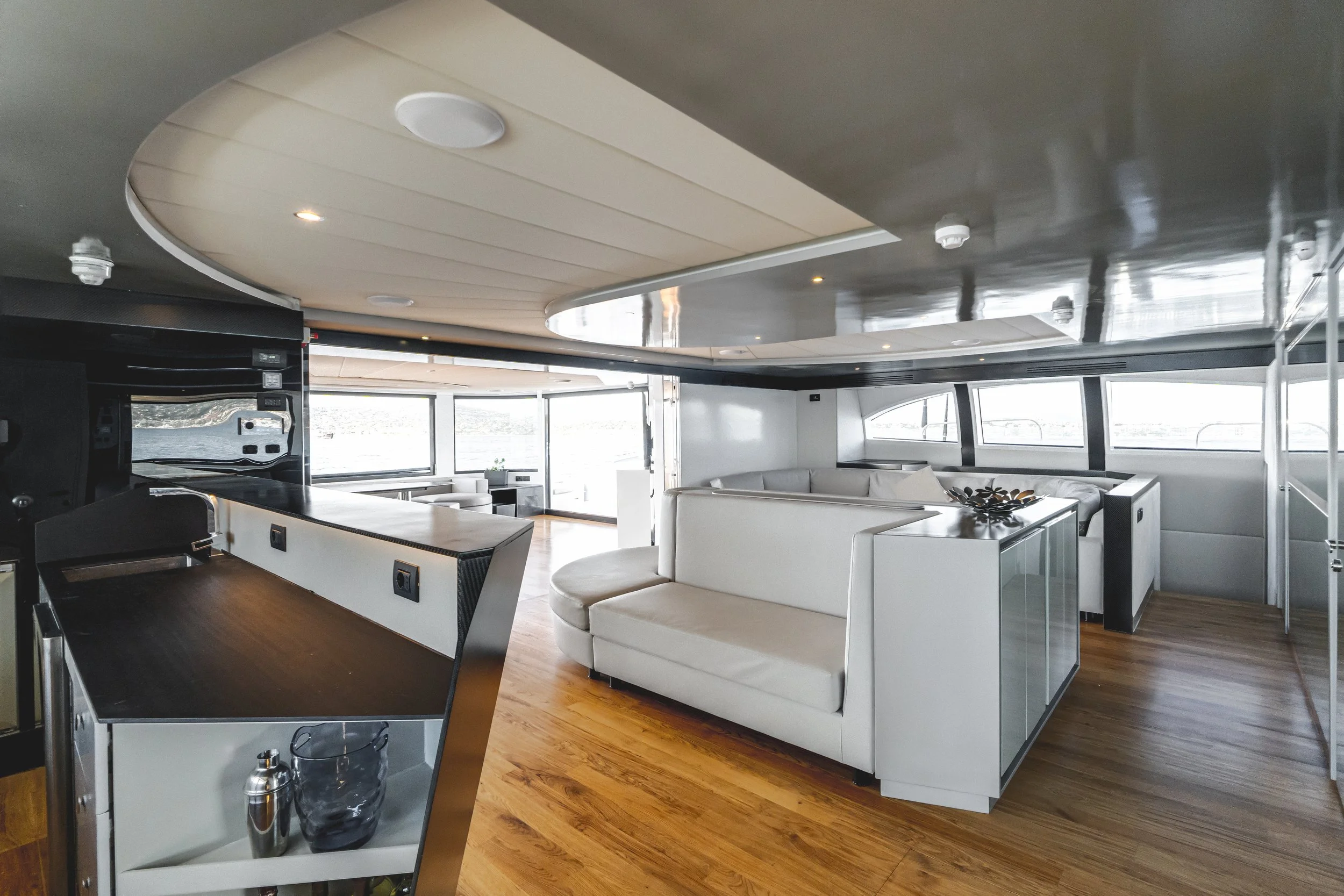 Modern yacht interior with white sofas, large windows, wooden flooring, and a sleek ceiling design. LYFE AT SEA