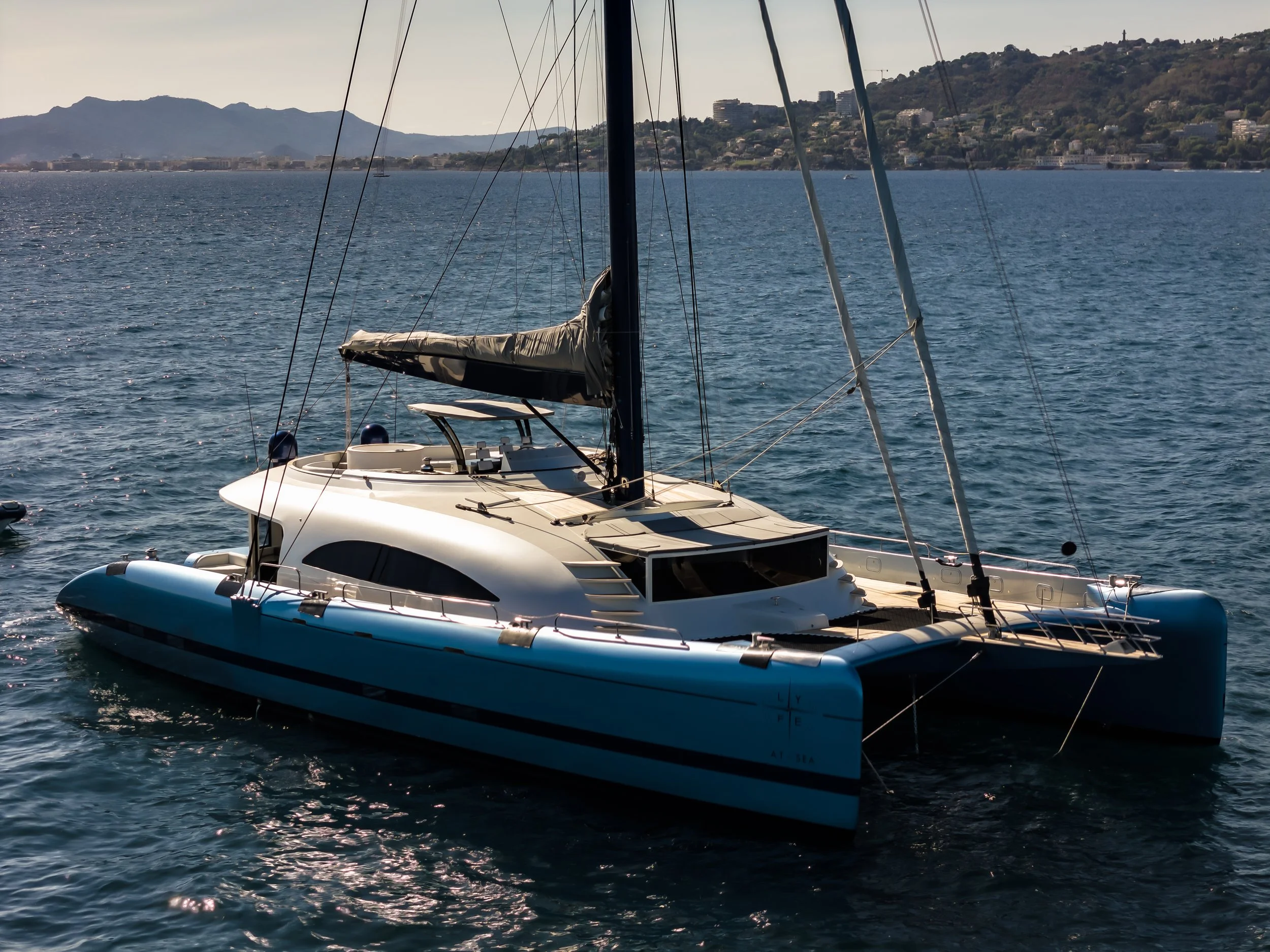 A sailboat on a body of water with a coastal city and mountains in the background.