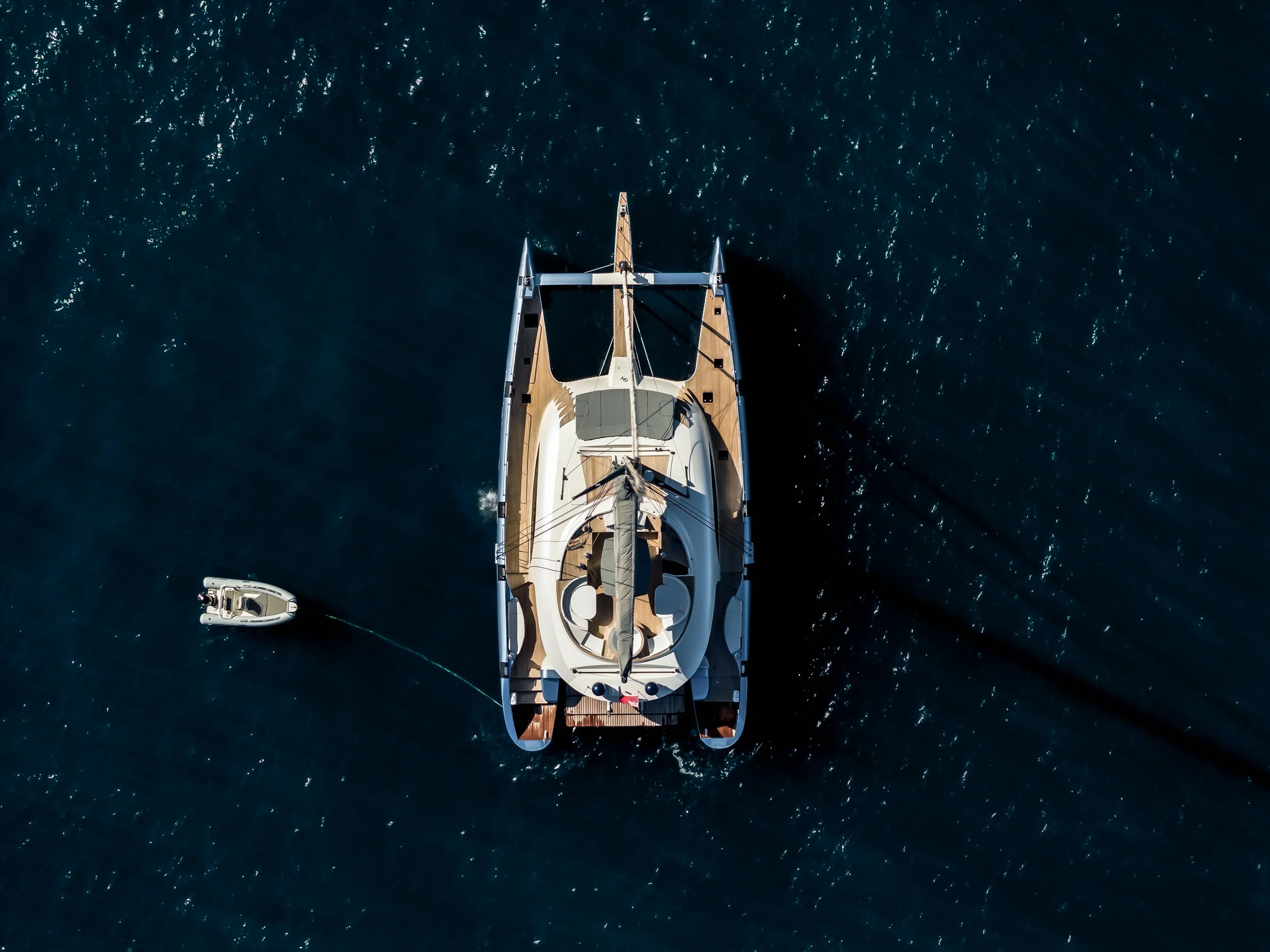 Aerial view of a luxury yacht sailing on open water, with a smaller boat nearby. LYFE AT SEA