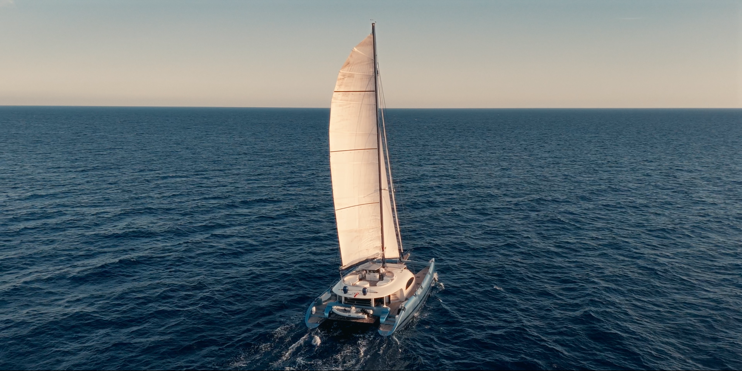 A sailboat with white sails sailing on the open ocean during daytime. LYFE AT SEA
