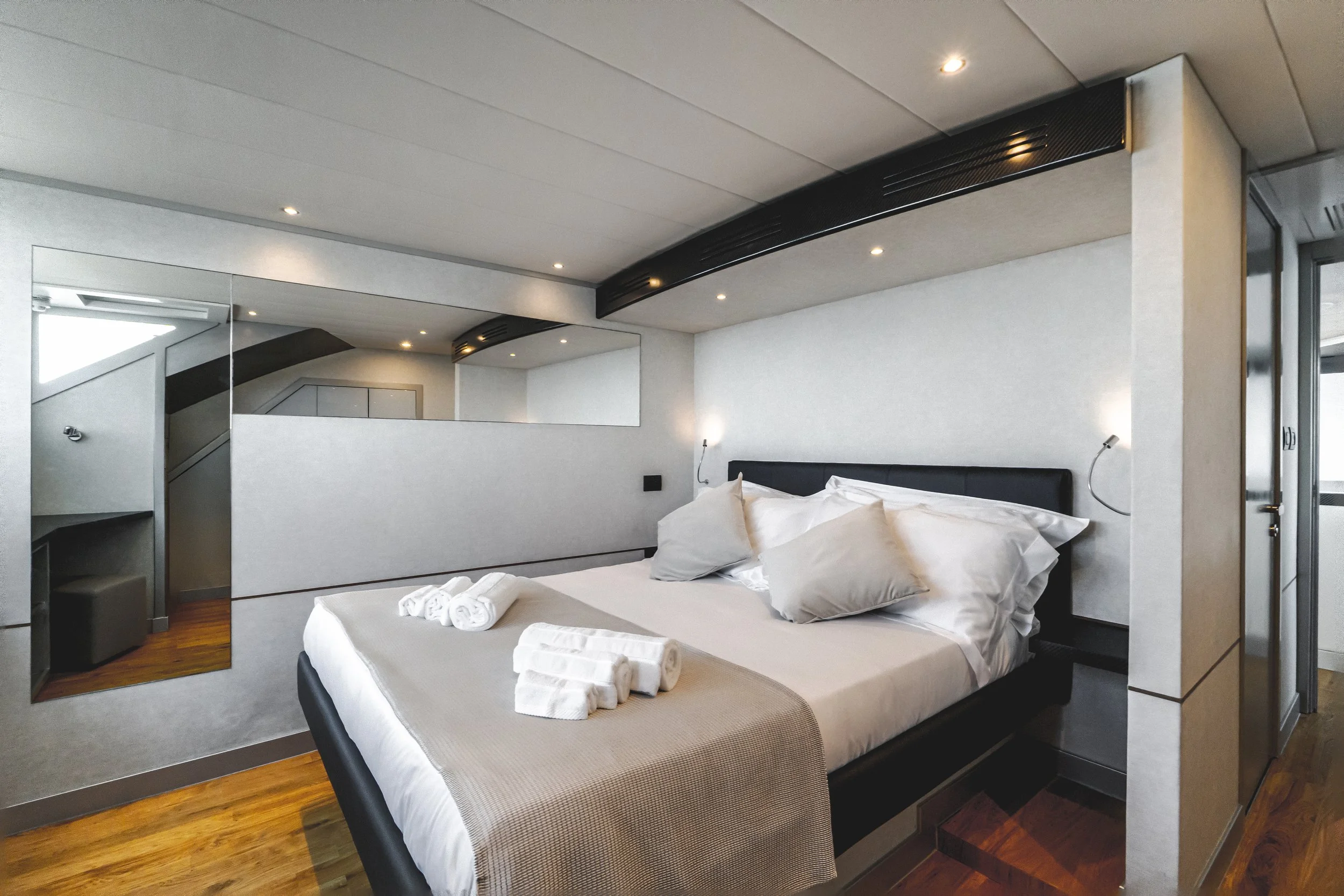 Modern hotel room with a large bed, neatly arranged with white linens and pillows, a towel art decoration, a mirrored wall, and minimalist lighting. LYFE AT SEA