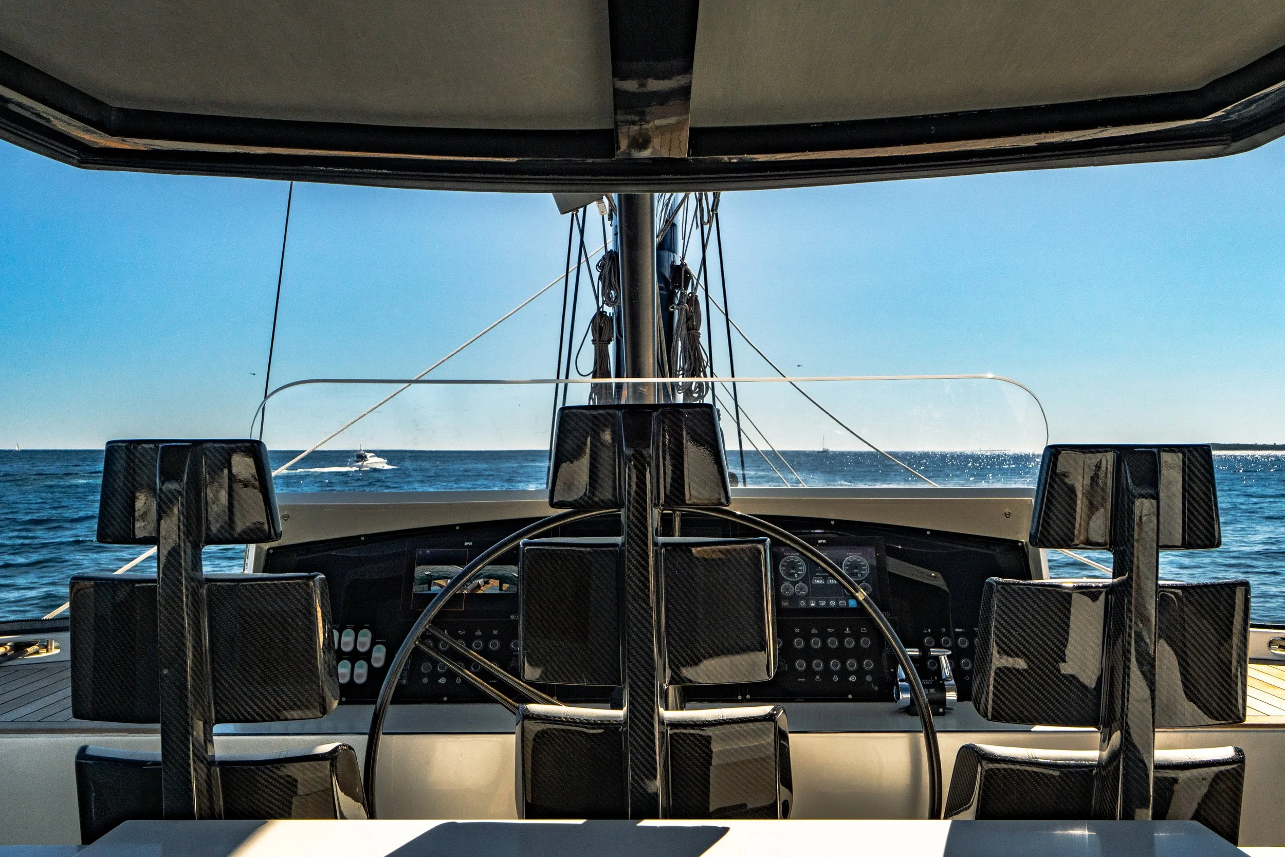 View from the helm of a yacht, showing the steering wheel, control panels, and seating, with the ocean and a boat visible in the background. LYFE AT SEA