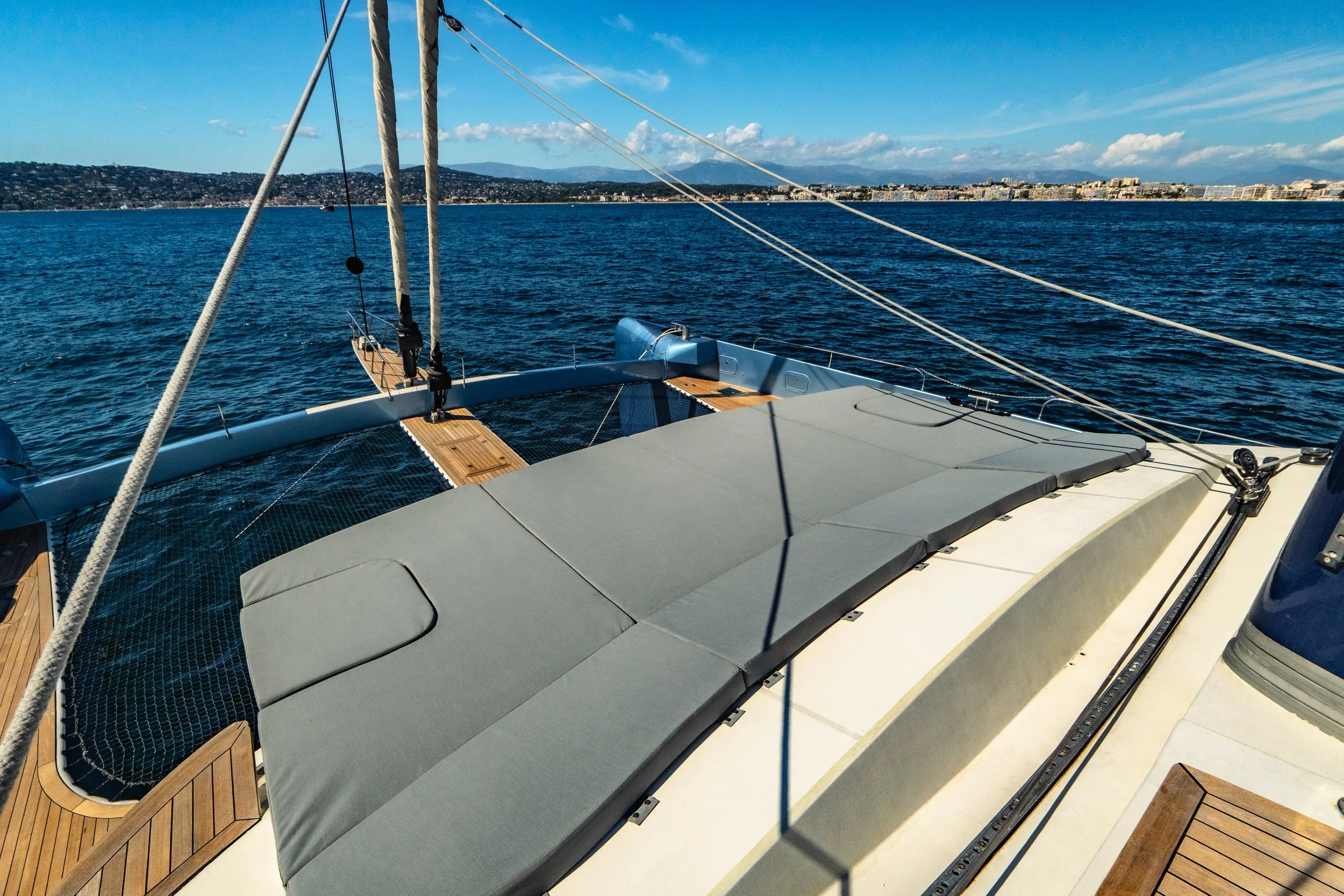 View from the deck of a sailboat showing the ocean with a distant city skyline and mountains in the background.