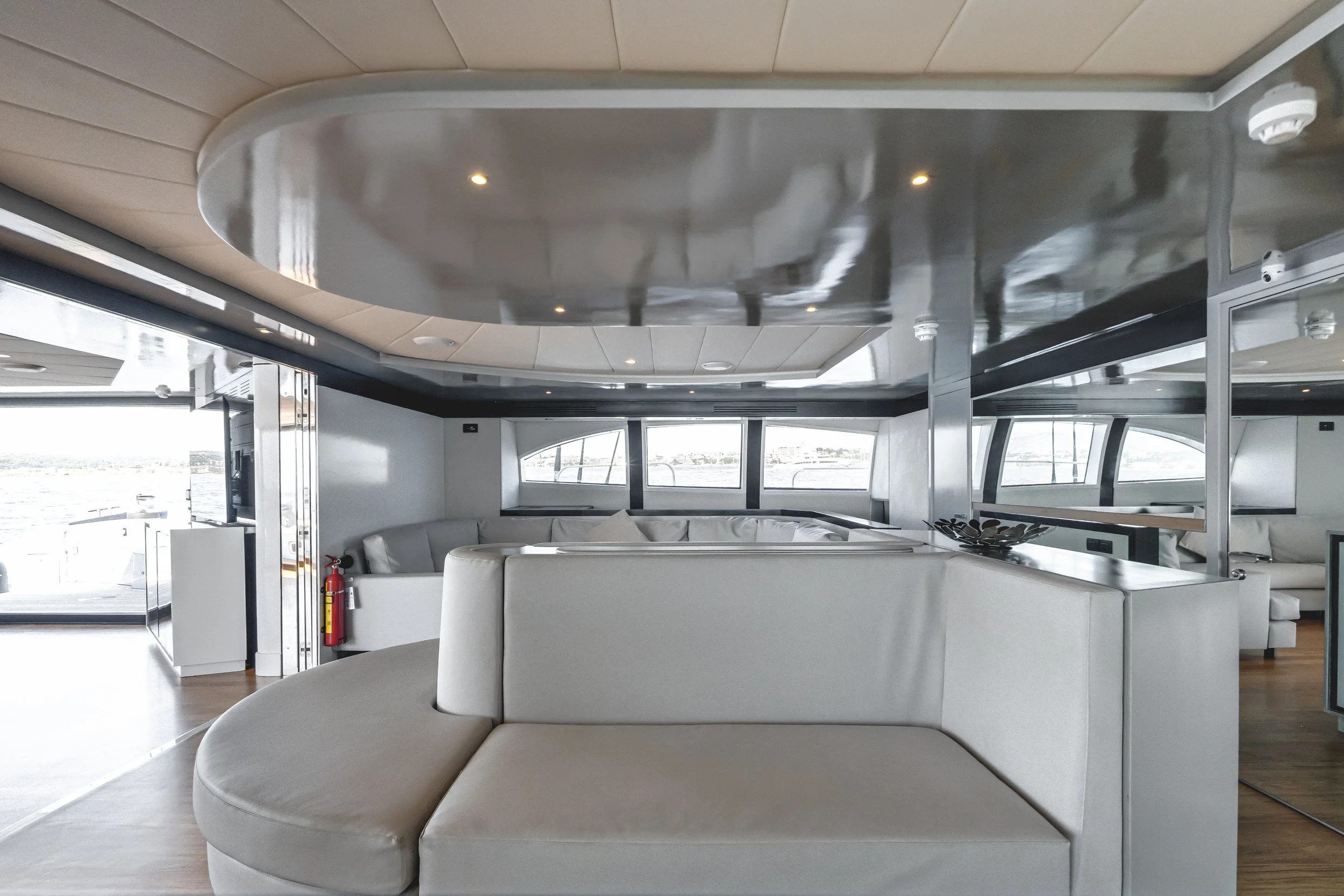Interior of a modern yacht with white seating, large windows, and a view of water outside. LYFE AT SEA