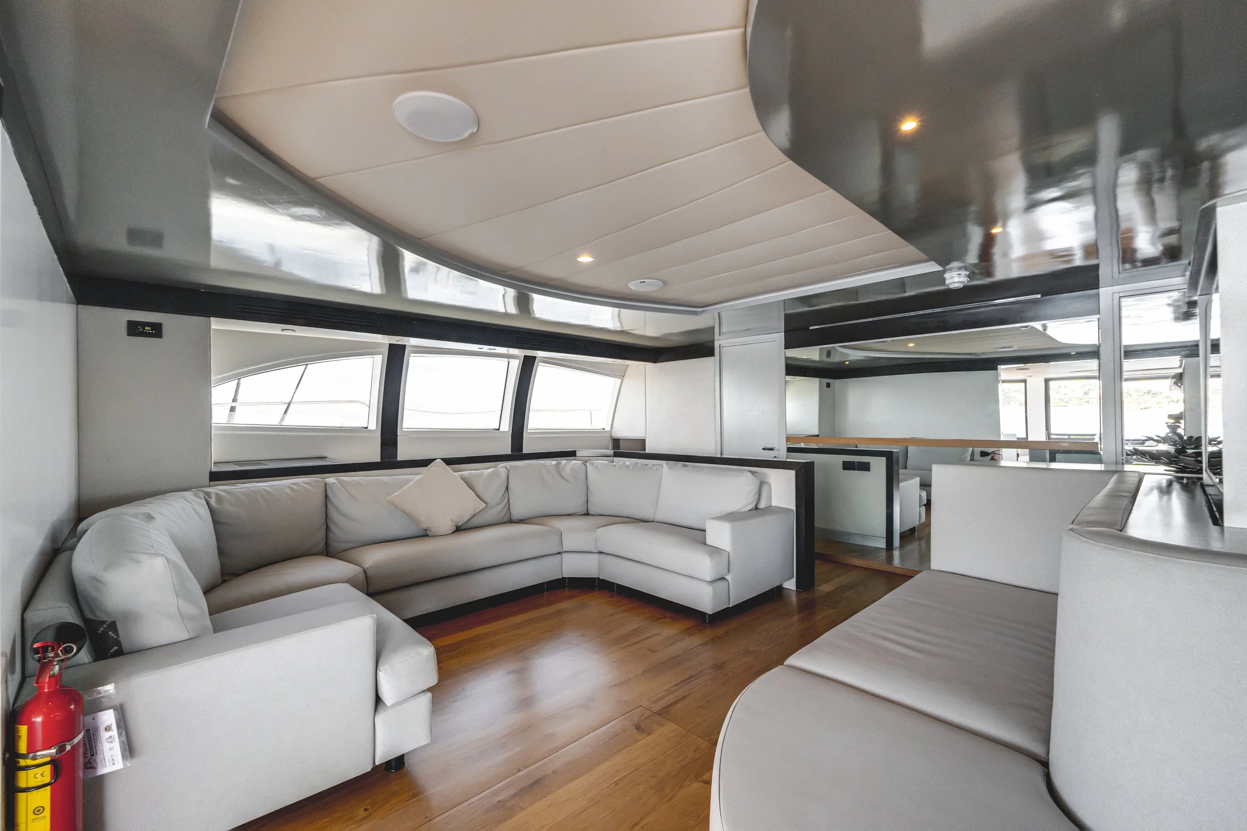 Indoor lounge area with curved white sofa, wooden flooring, large windows, beige and black ceiling design, and reflections on the ceiling. LYFE AT SEA
