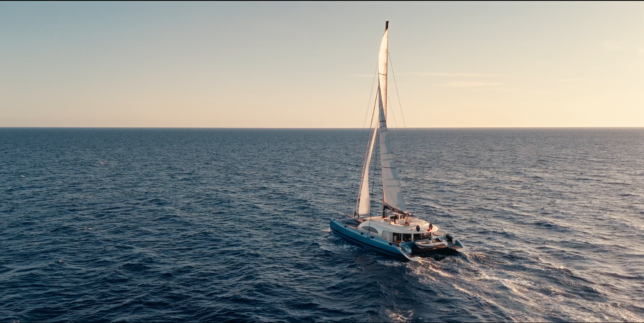 A sailboat with a white hull and sails navigating on a calm ocean during sunset. LYFE AT SEA