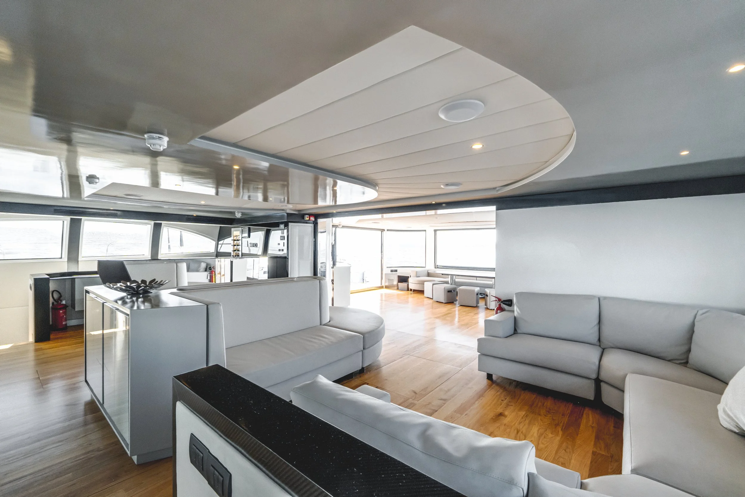 A spacious, modern living area with white sofas, wooden flooring, large windows, and a curved ceiling with recessed lighting.LYFE AT SEA
