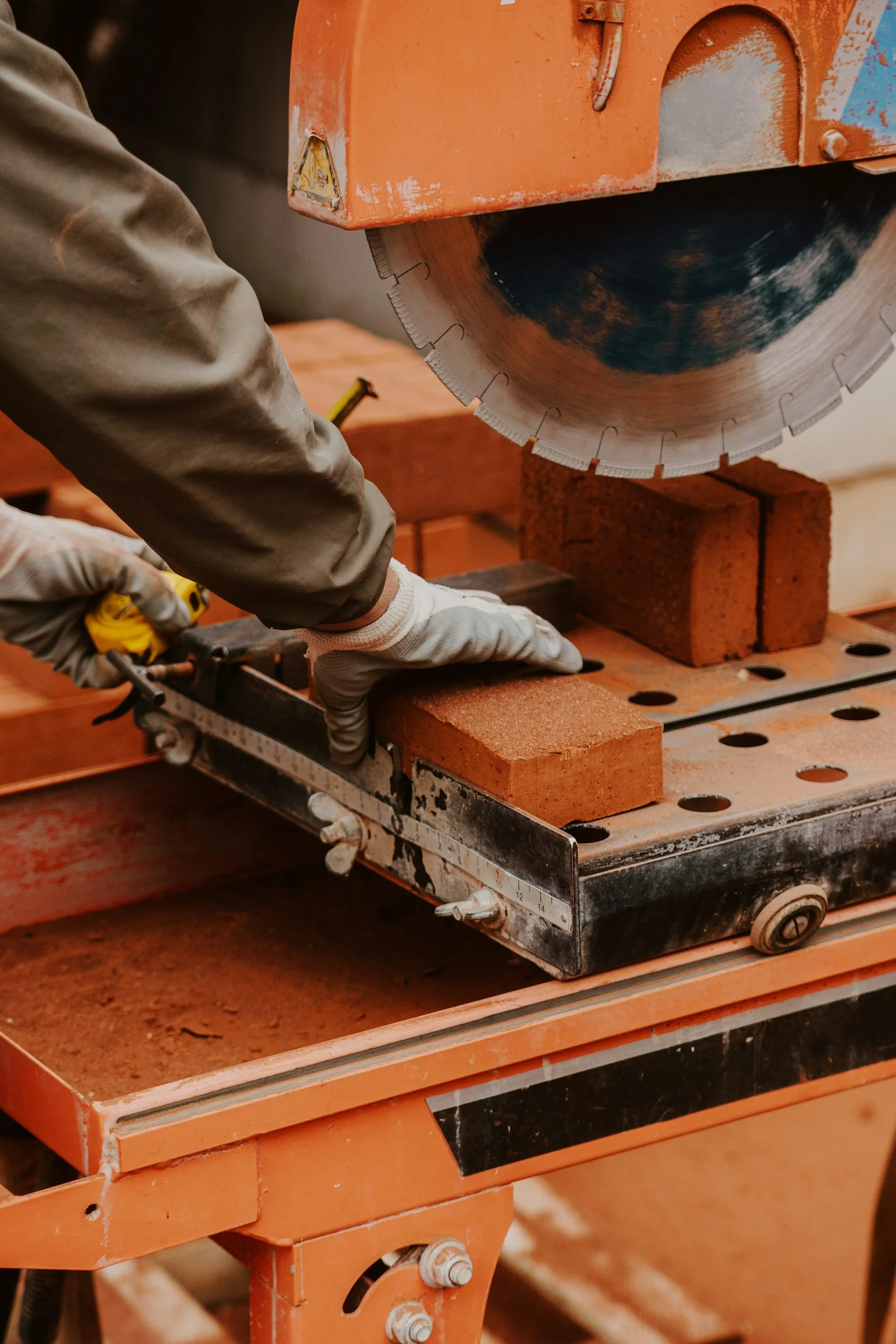 Close-up of a person cutting bricks with a large industrial circular saw on a metal work table.