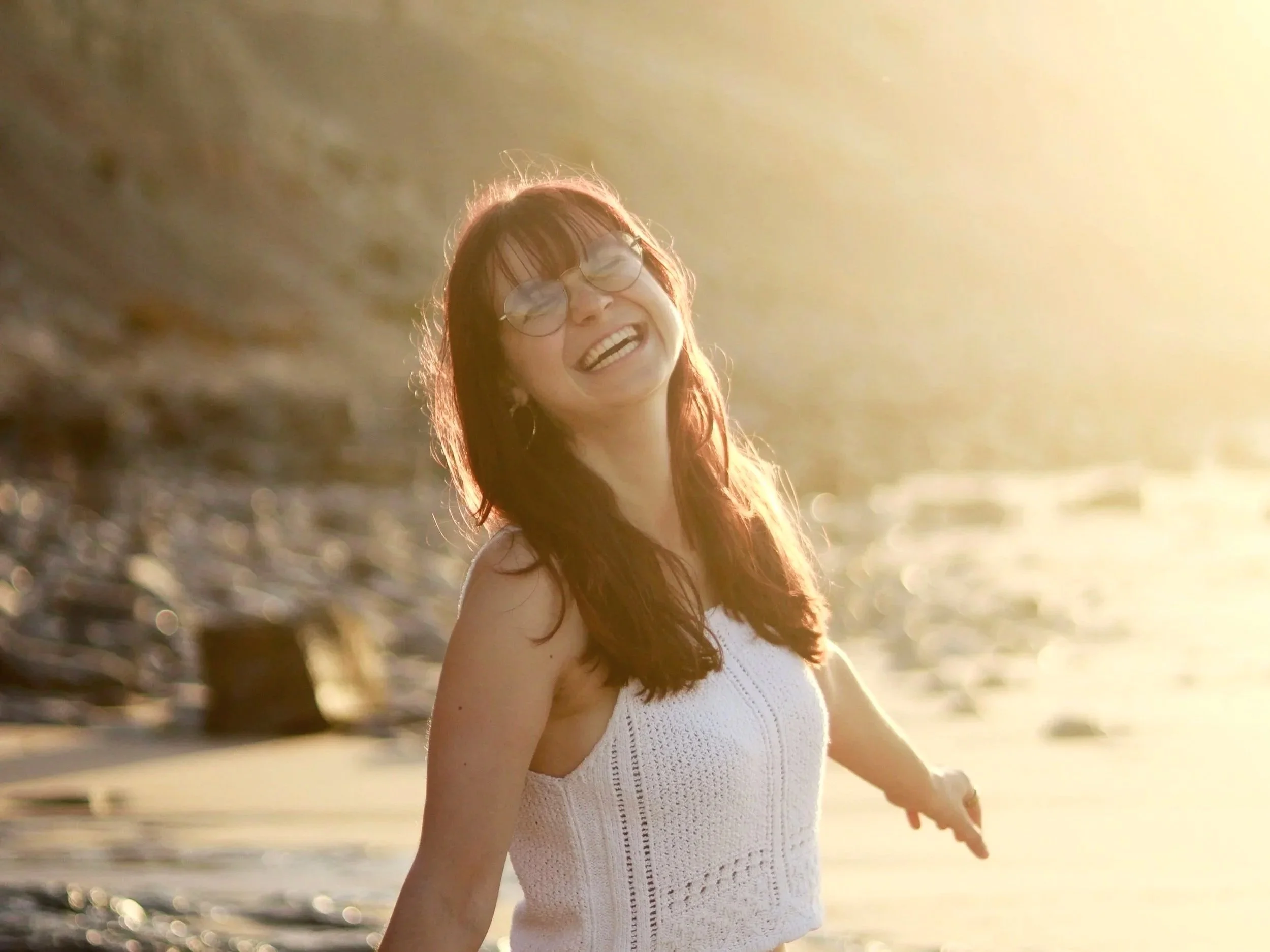 Vrouw met bril glimlachend op het strand bij zonsondergang.