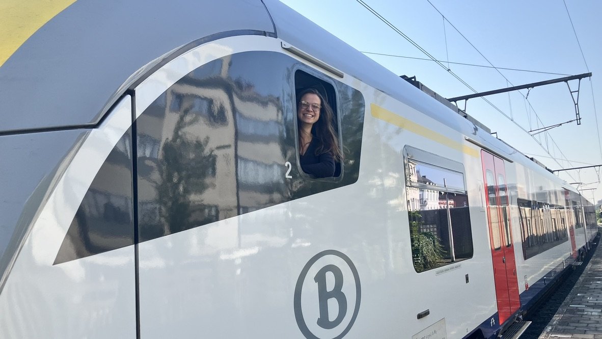 Vrouw die uit het raam van een moderne trein kijkt en glimlacht.