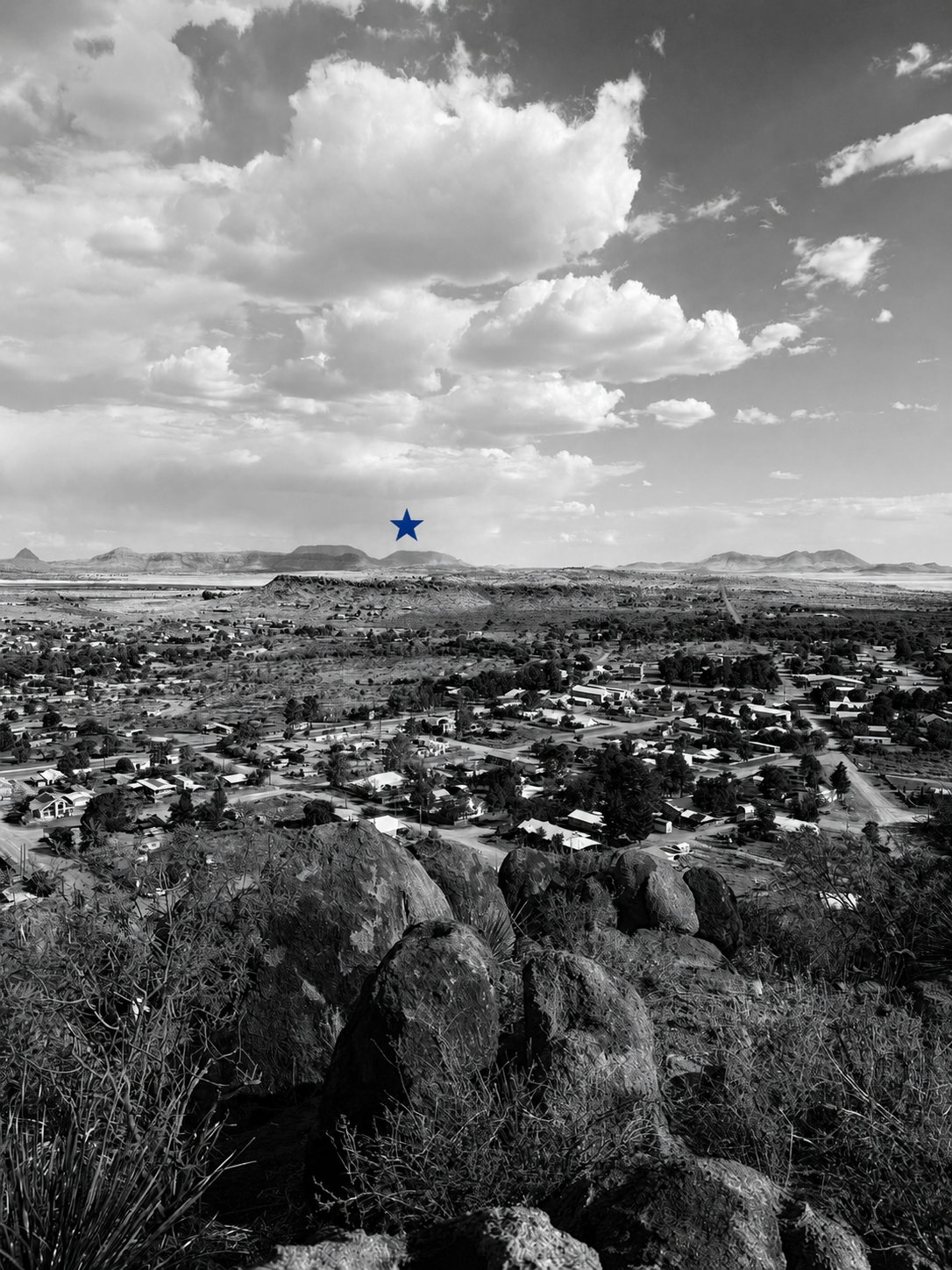 A black and white landscape photo overlooking the town of Fort Davis, Texas with the Sleeping Lion mountains in the background, highlighted with The Sleeping Lion blue star.