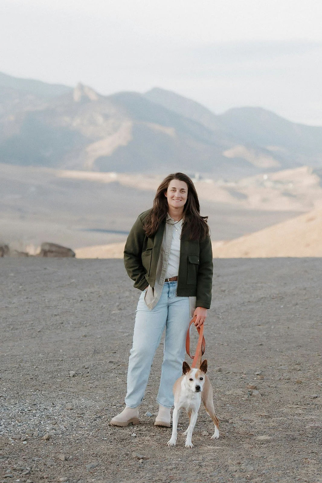 Evelyn Iacono standing on a dirt landscape holding a dog on a leash with mountainous terrain in the background.