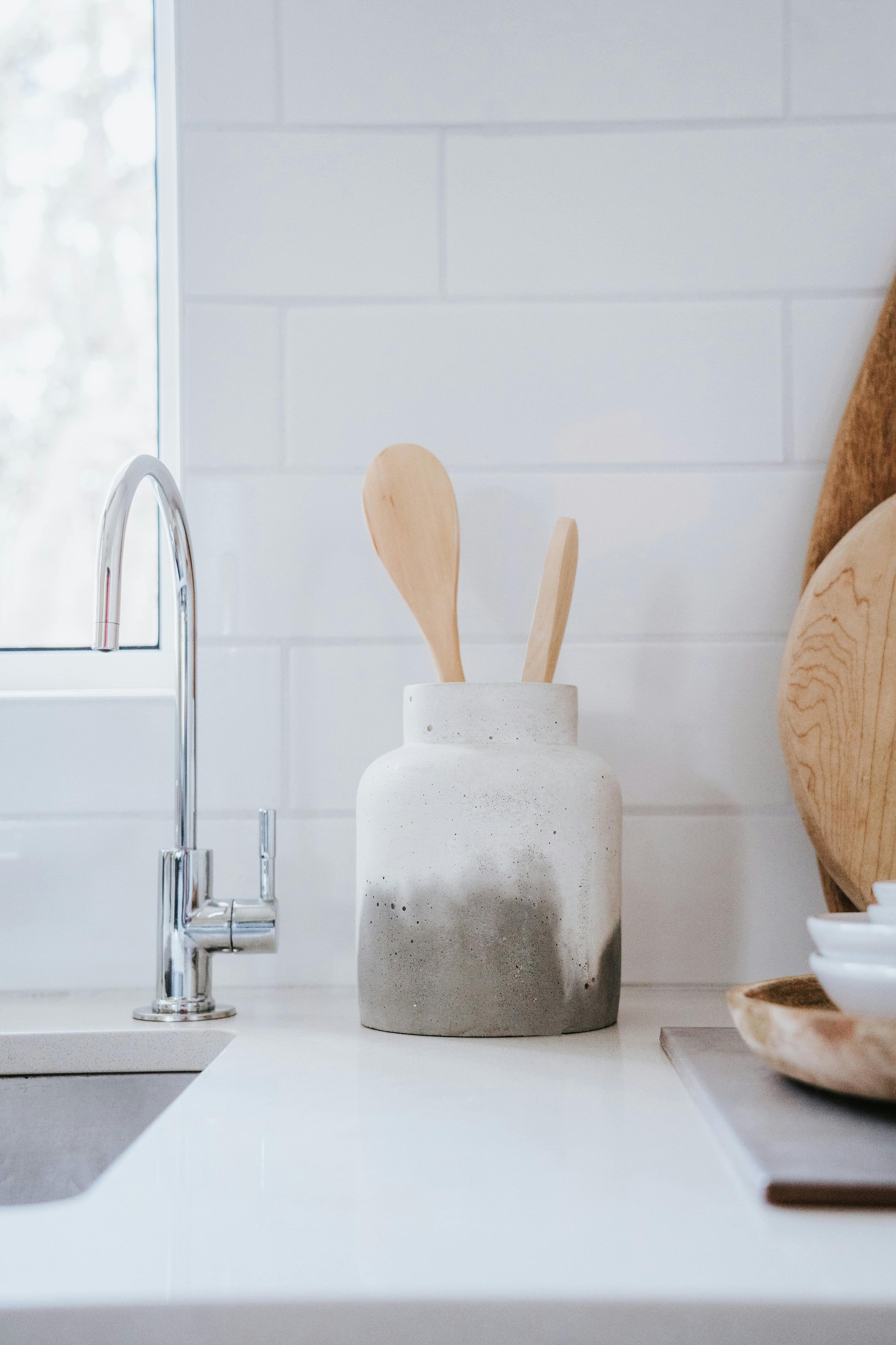 Close-up of a kitchen countertop with a concrete vase holding wooden utensils, a marble tray, and a bowl, near a window with white frames. Kitchen reset in a home managed by Lighter Home household management service in Gainesville, Florida