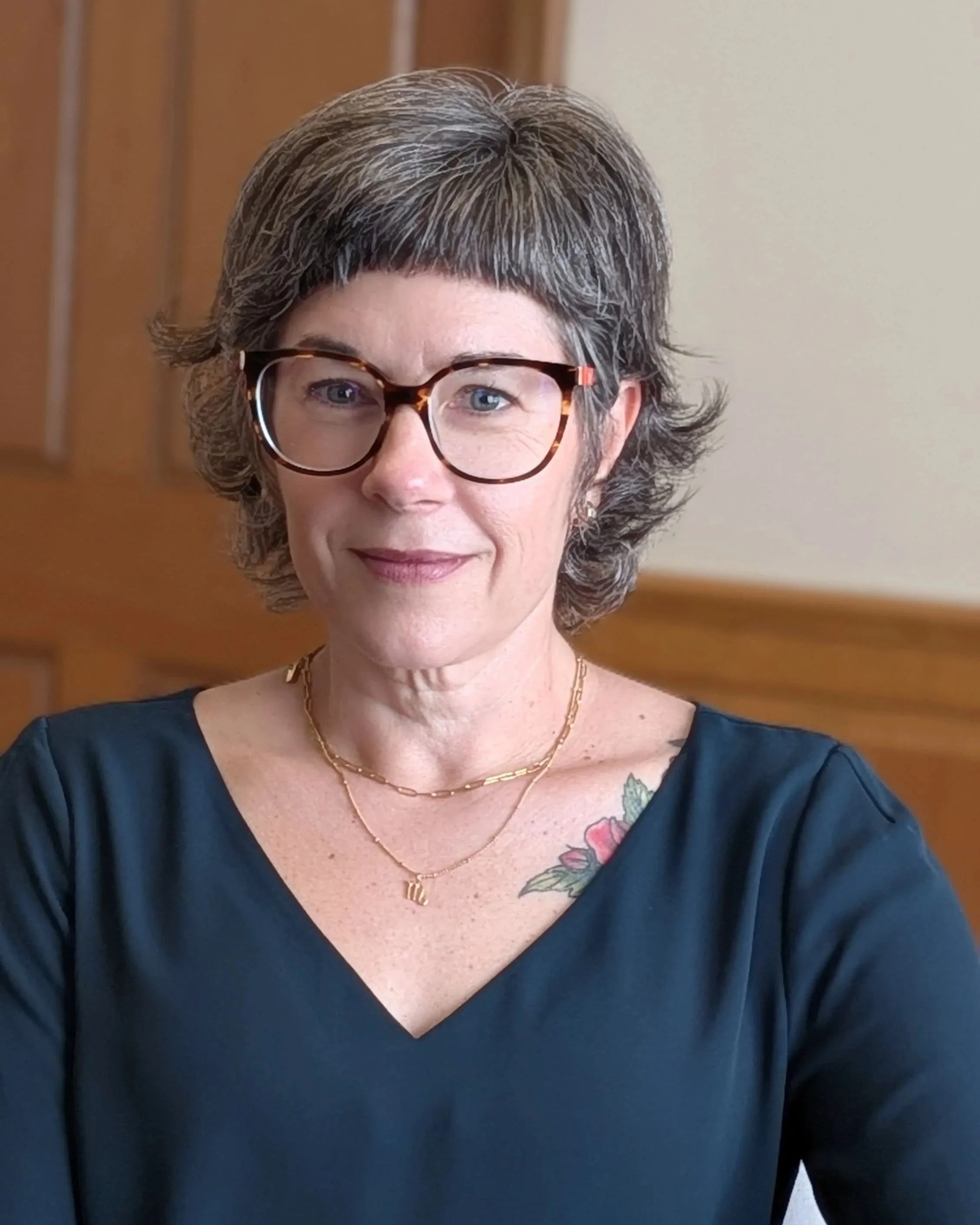 Close-up photo Lighter Home founder Colleen Raccioppi. She is a smiling woman with short, gray and black hair, wearing tortoiseshell glasses, gold necklaces, and a dark green top.