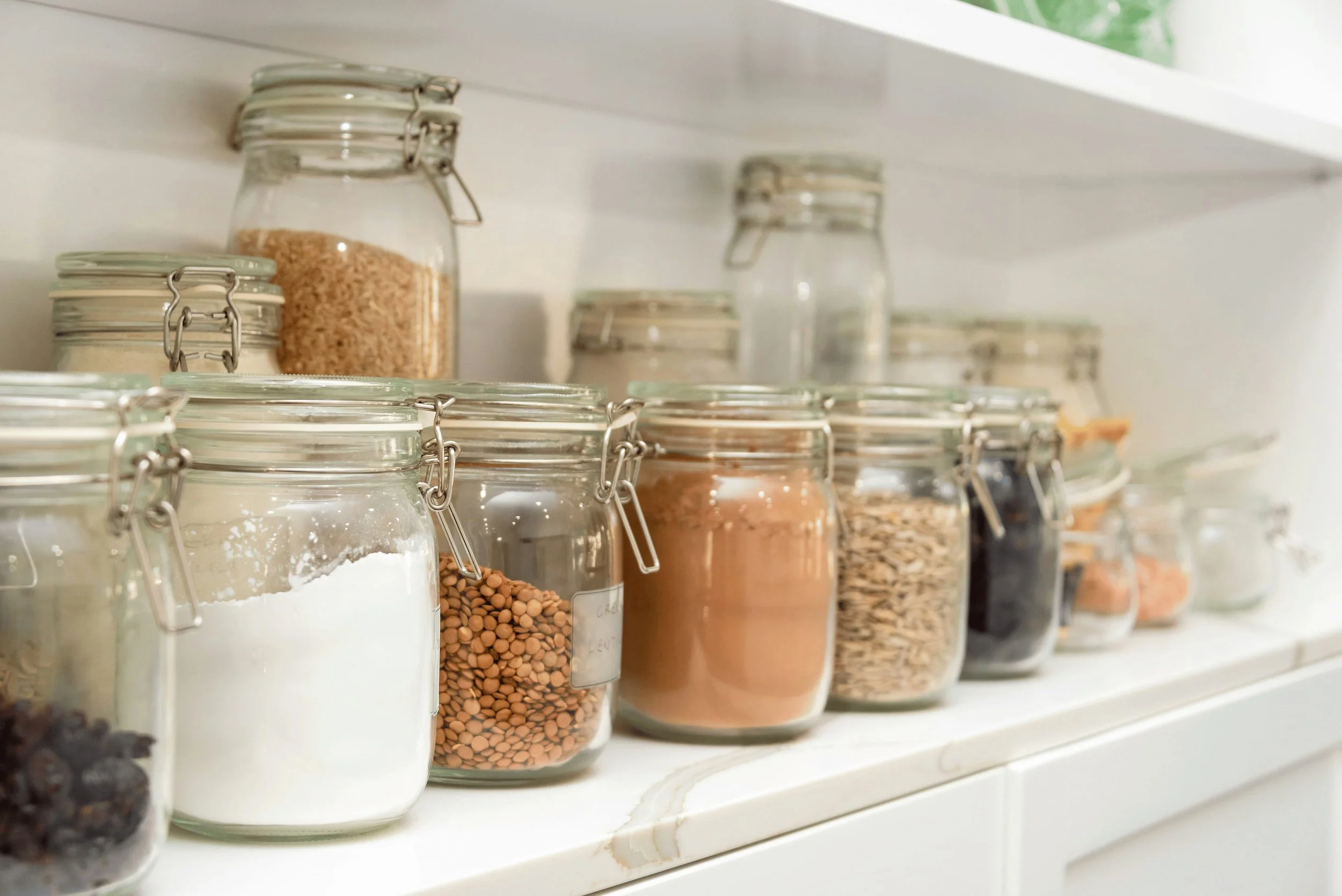 A pantry shelf with multiple glass jars containing various spices, grains, and dried foods in an organized kitchen setting. Pantry upkeep and management included in Lighter Home weekly household management service Gainesville Florida