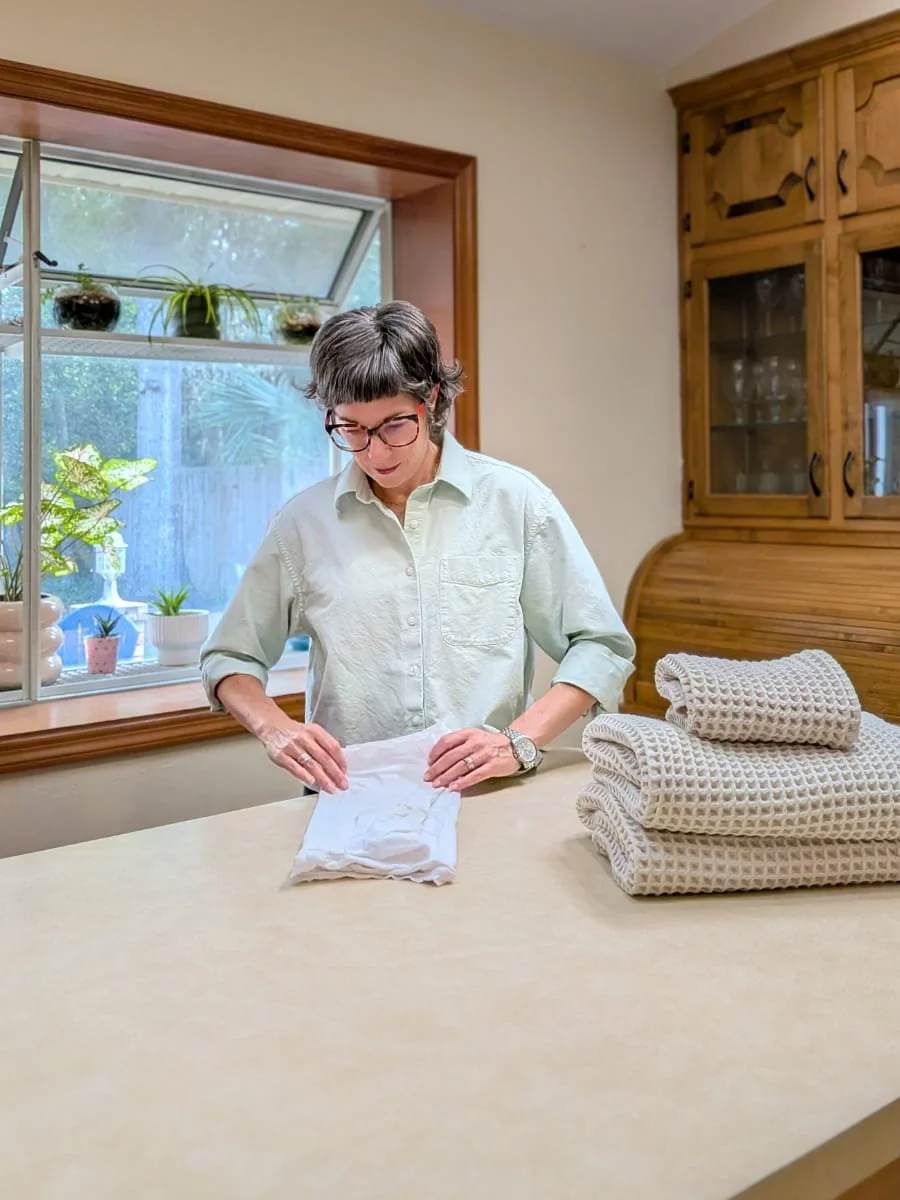 Lighter Home owner Colleen Raccioppi folding laundry at a kitchen counter in Gainesville Florida — household management service handling weekly laundry for busy professional families.
