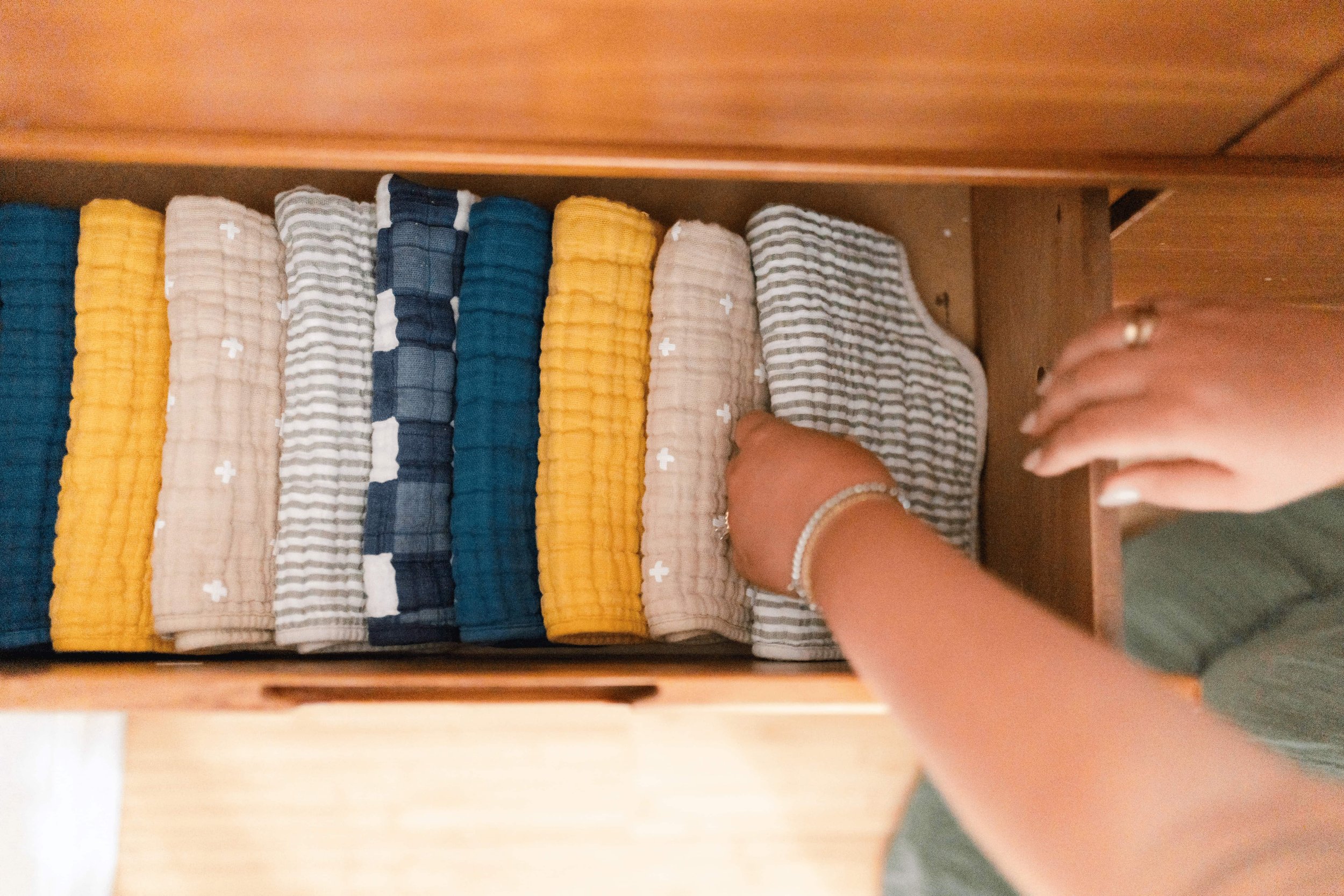 A person's hands reaching into a drawer filled with neatly folded cloths in various colors and patterns. Laundry managed by Lighter Home household management in Gainesville, FL.