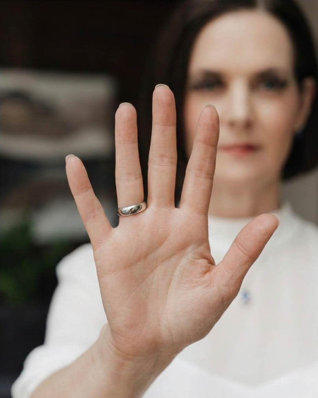 A woman with dark hair showing her hand with a silver ring as she holds up her palm towards the camera.