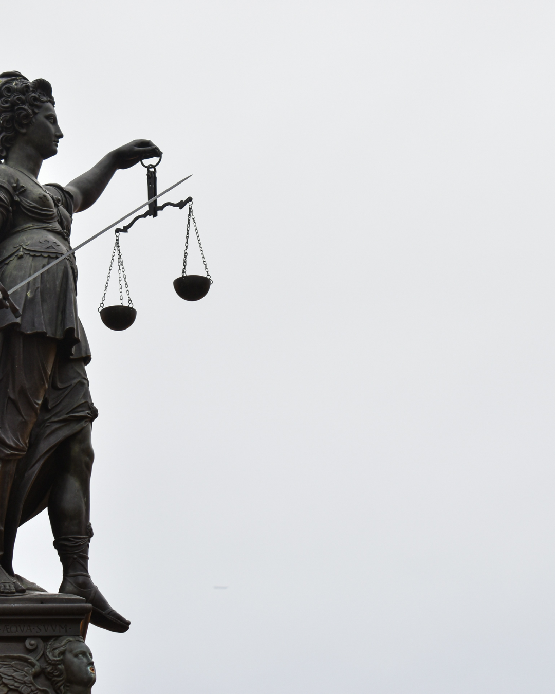 Statue of Lady Justice holding scales against a cloudy sky.