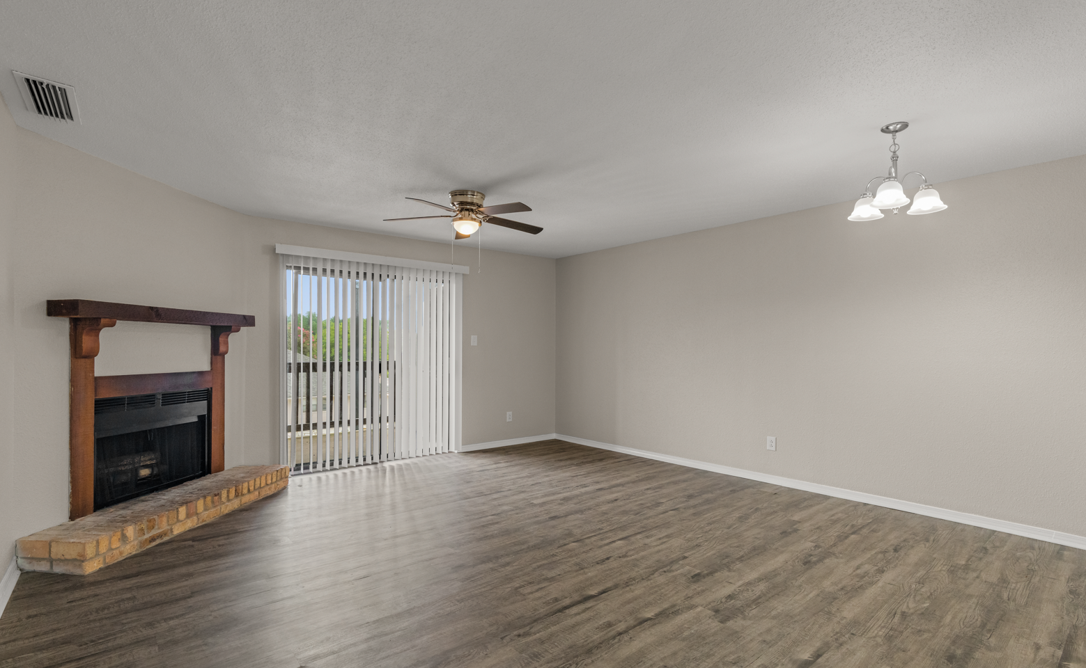 Empty living room with fireplace, sliding glass door with vertical blinds, ceiling fan, and chandelier