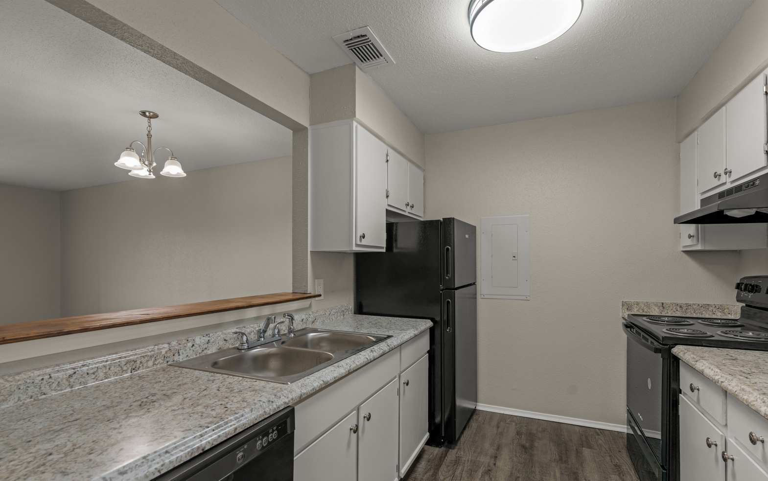 Kitchen with off-white cabinets, granite countertops, black refrigerator, black stove, and sink with a view into a living area with a hanging light fixture.