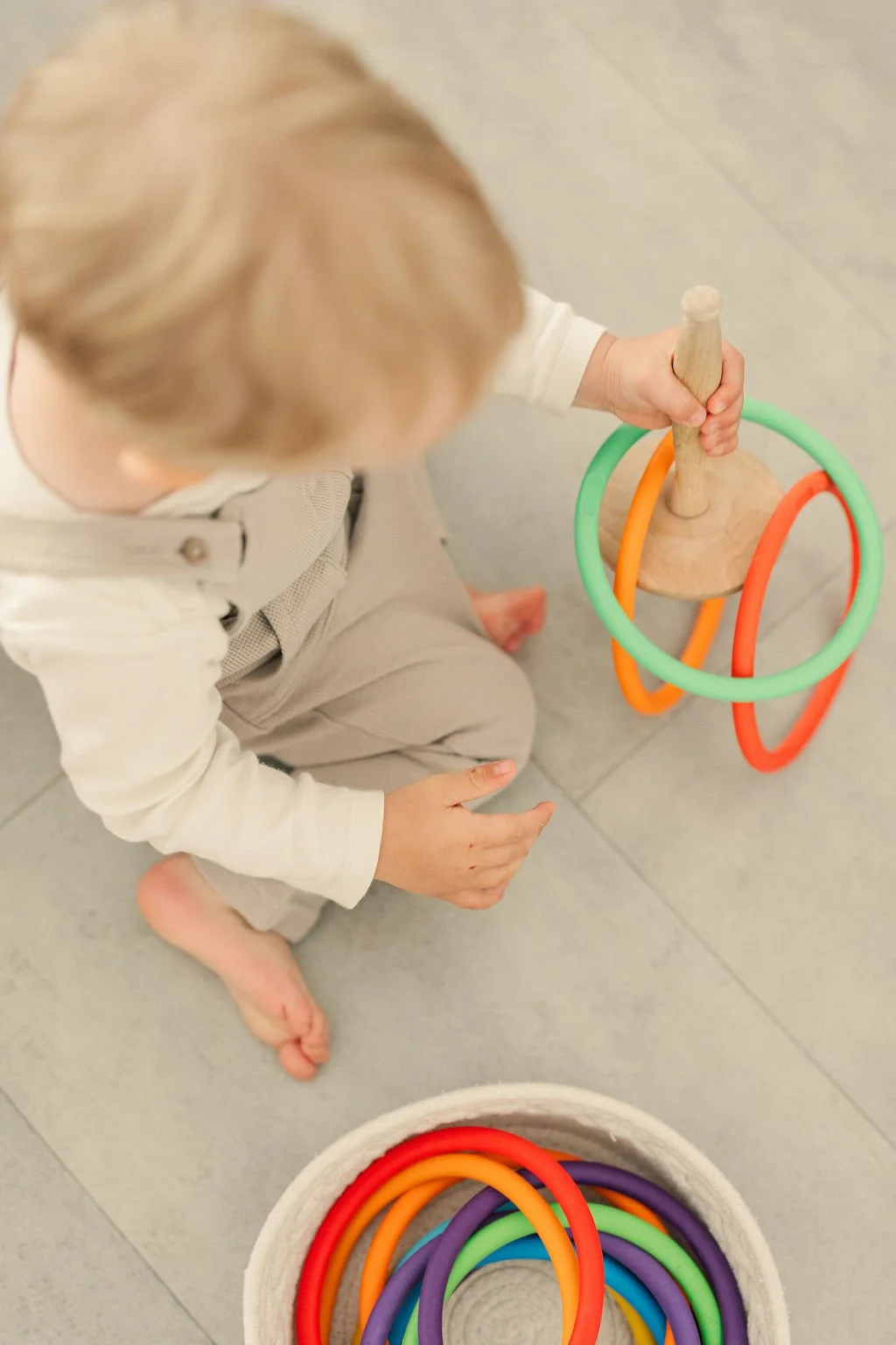 Ein Kind sitzt barfuß auf einem Boden und spielt mit bunten, flexiblen Ringen, die in einer Schüssel liegen.