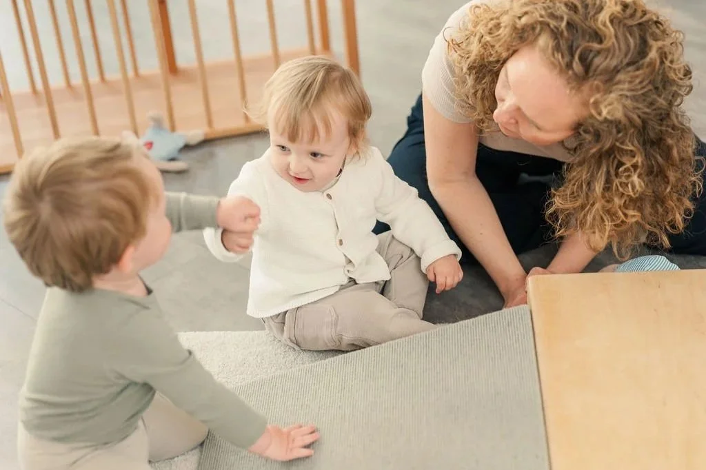 Drei Kinder und eine Frau spielen gemeinsam auf dem Boden in einem Raum
