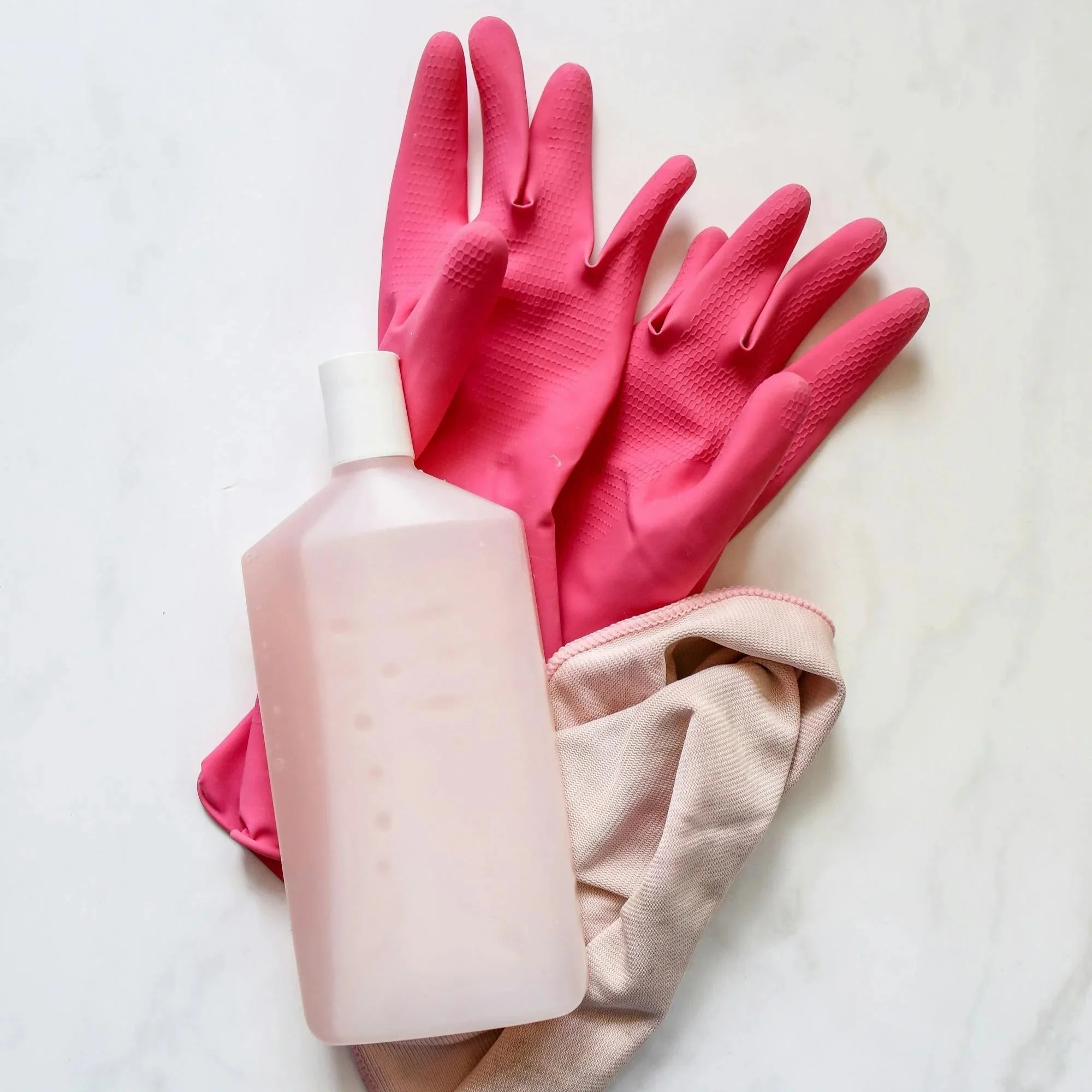 A pair of pink rubber gloves resting on a beige fabric and a white surface.