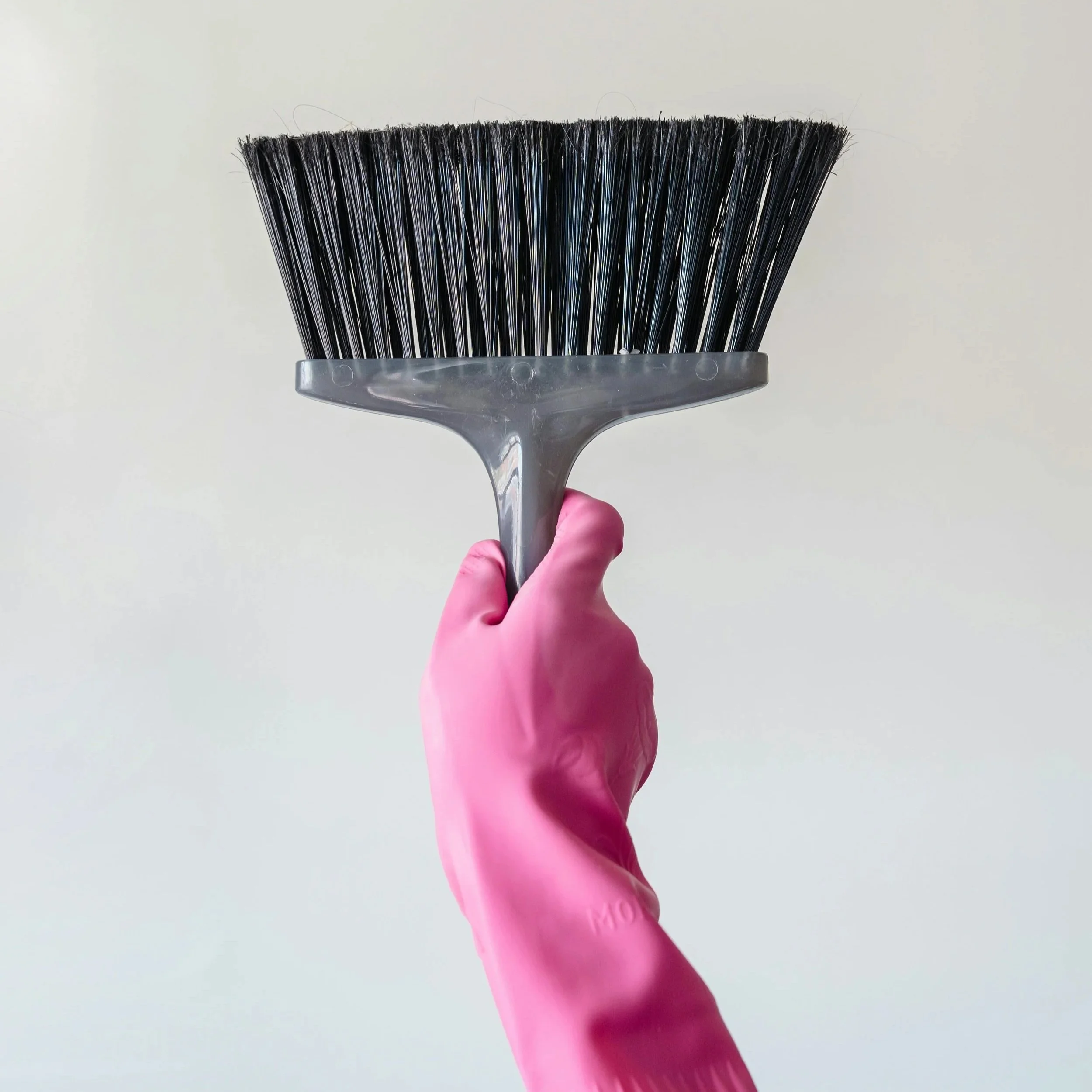 Close-up of a black hairbrush with plastic bristles being held by a person wearing a pink glove against a plain white background.
