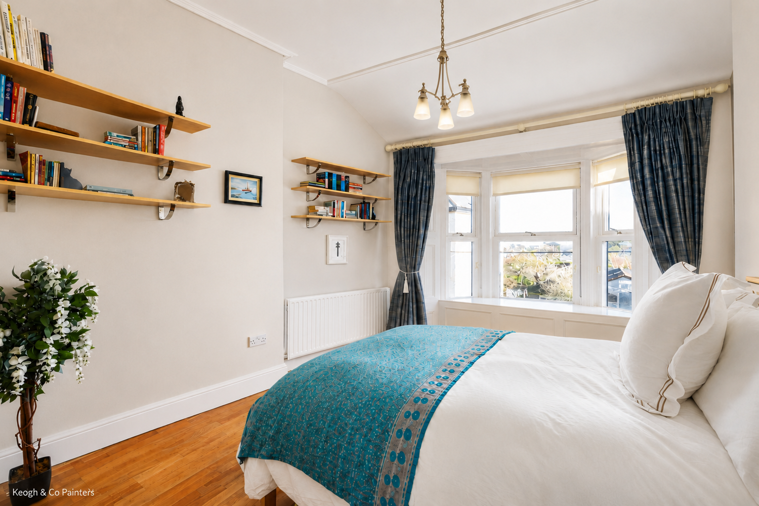 A bedroom with white walls, a wooden floor, a bed with white bedding and blue accents, large bay windows with blue curtains, wall-mounted bookshelves with books and decorative items, and a potted plant.