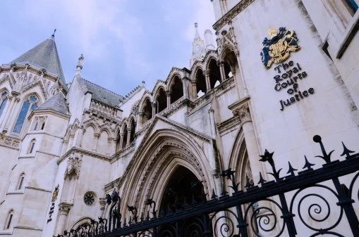 Exterior view of the Royal Courts of Justice building with ornate gothic architecture, crest, and black wrought iron fence.