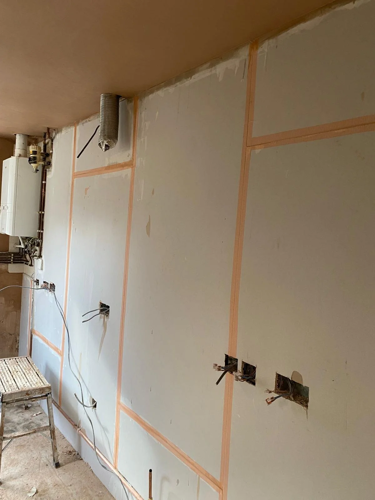 Interior wall under construction with electrical outlets and wiring, framed with orange construction tape.