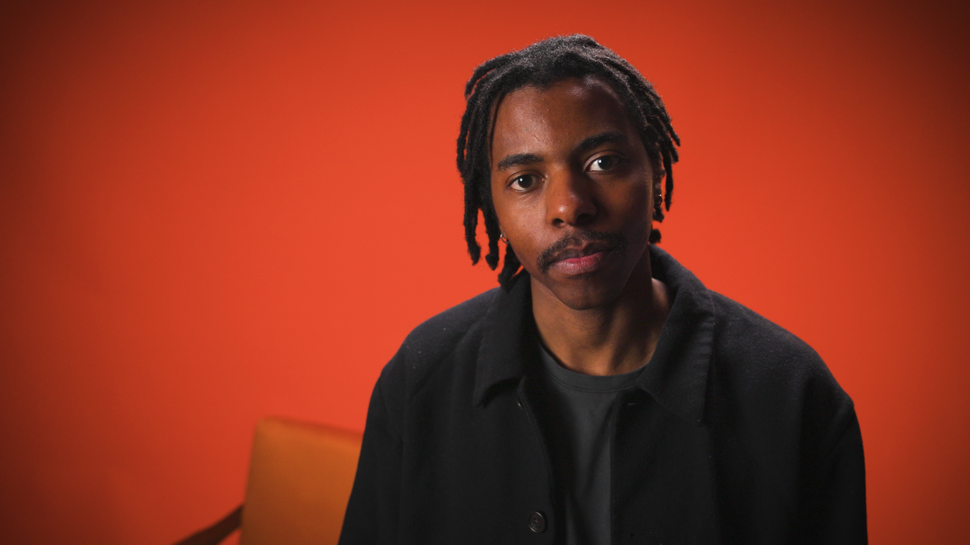 Musician standing in orange studio setting looking at camera for a music video