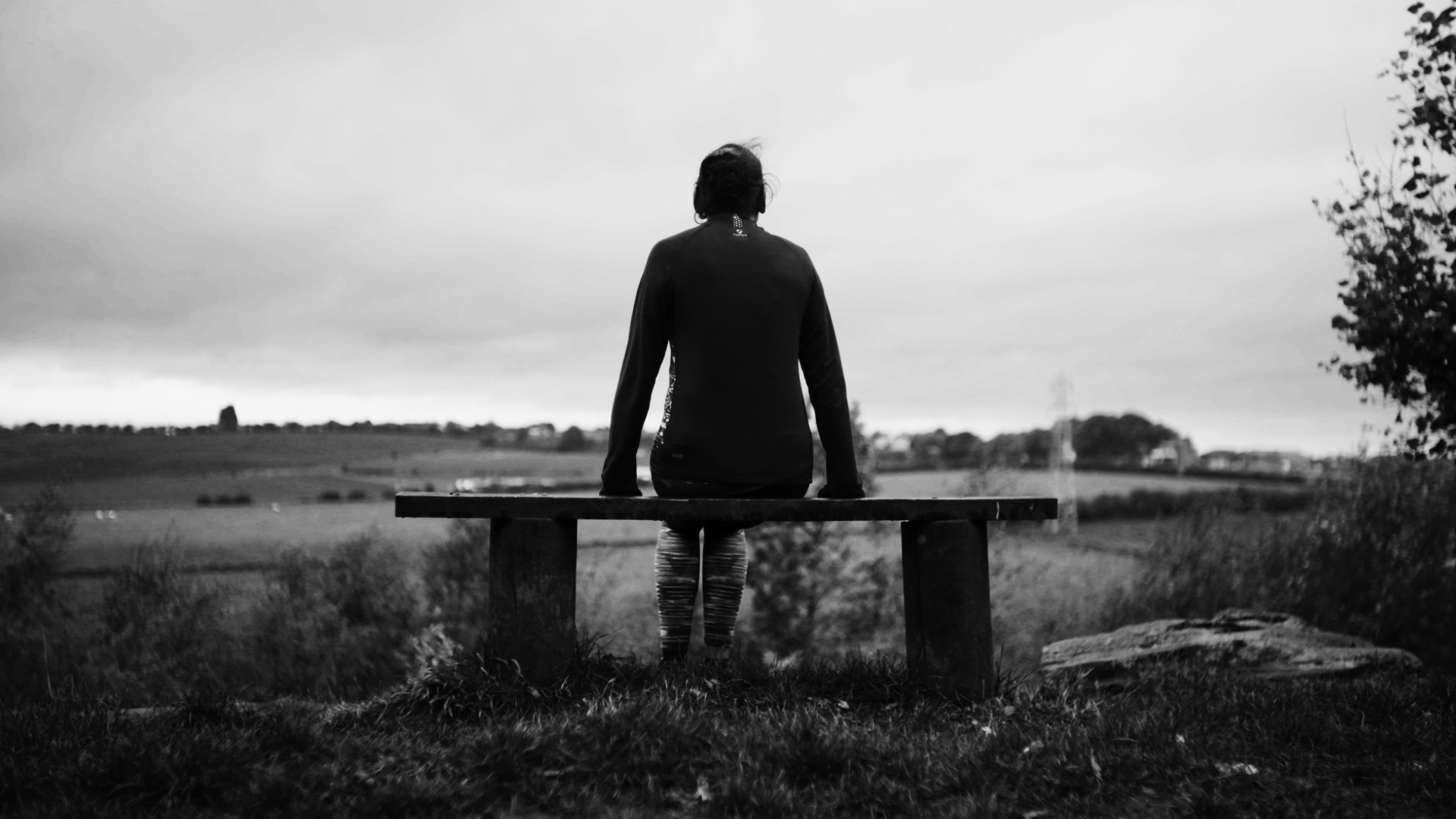 Documentary shot of a woman sat on a bench looking lonely and staring to the landscape behind