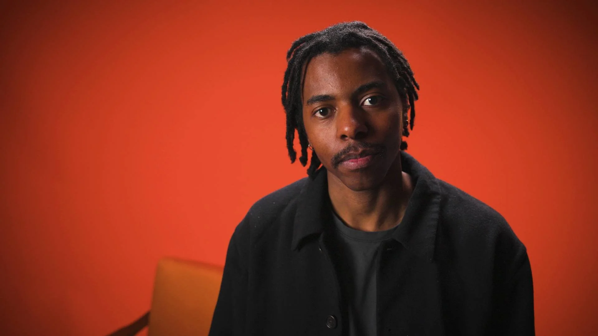 Musician standing in orange studio setting looking at camera for a music video